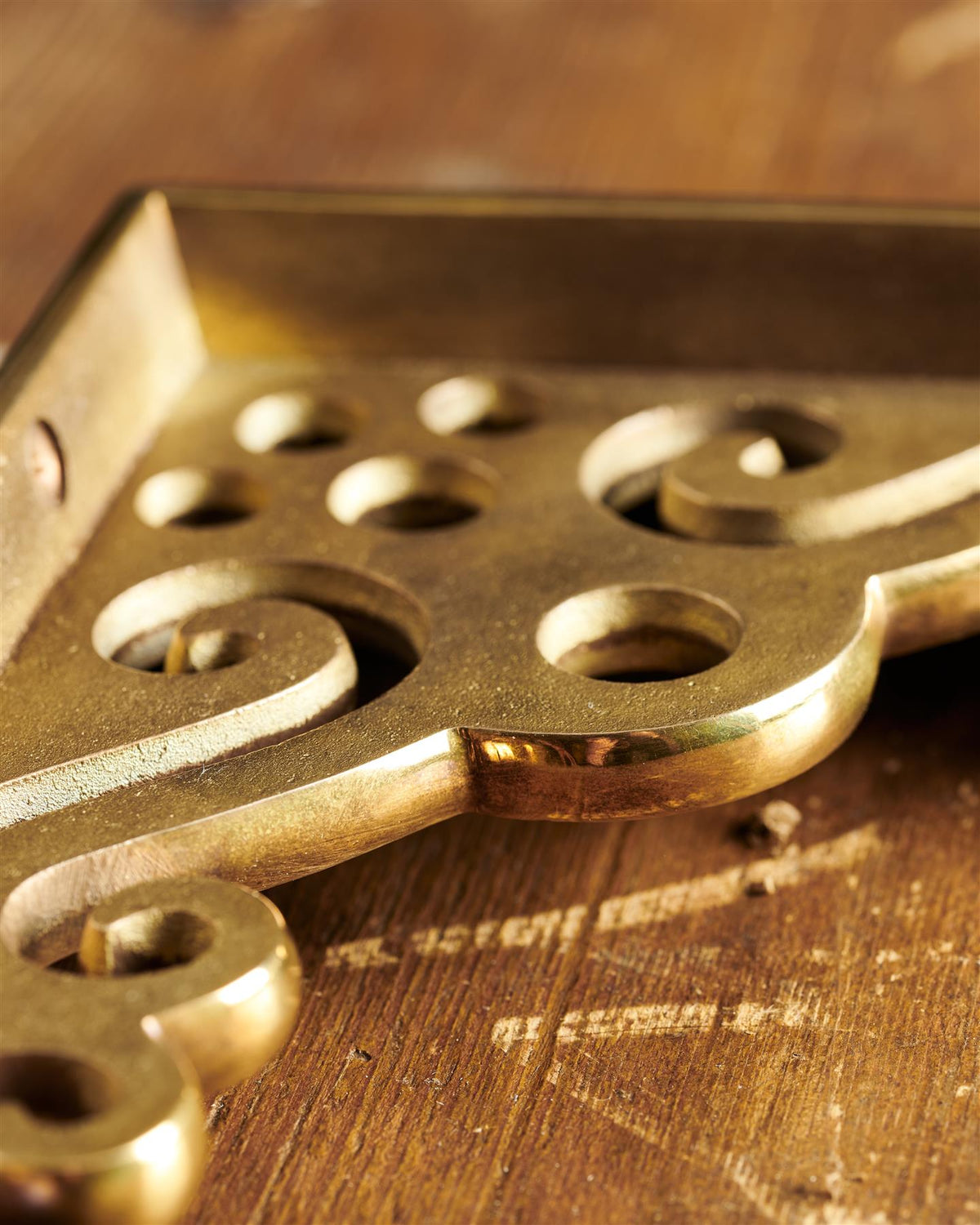 A close-up view of the decorative cutout patterns on a large Victorian-inspired ornate aged brass shelf bracket. TEST