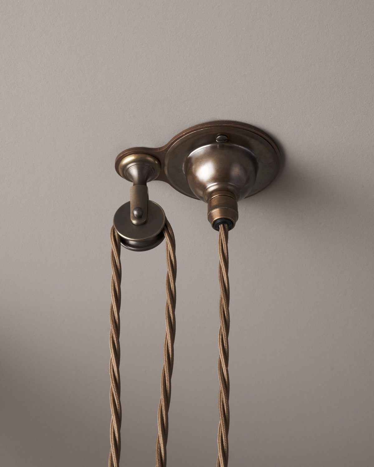 A small aged brass ceiling rose with a wheel pulley and a brown twisted fabric flex cord. TEST