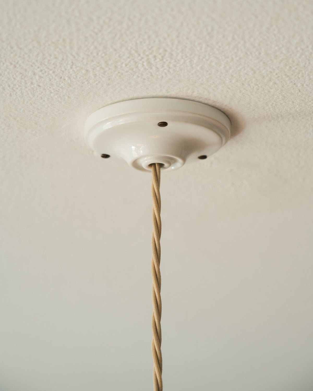 A white ceramic ceiling rose with cream twisted fabric flex cord. TEST