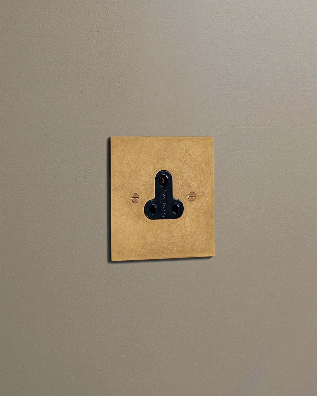 An oblique view of a classic 5 amp single plug socket in a mottled aged brass finish. TEST