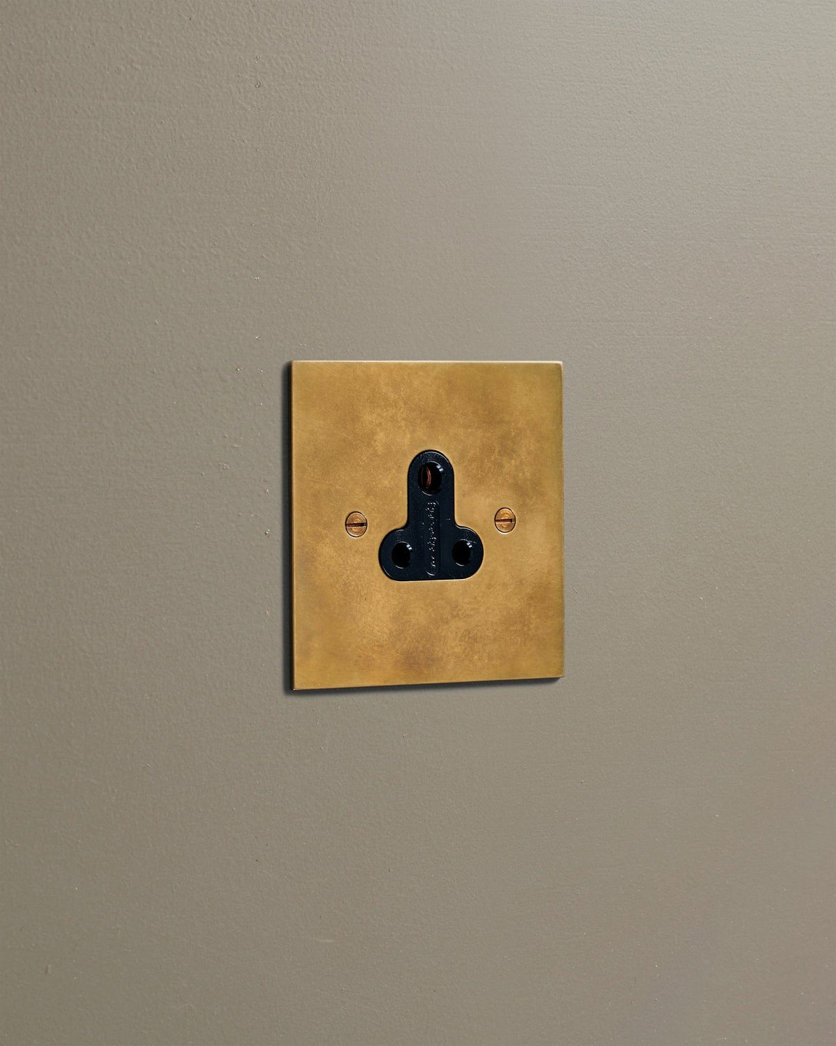 An oblique view of a classic 5 amp single plug socket in a warm burnished brass finish. TEST