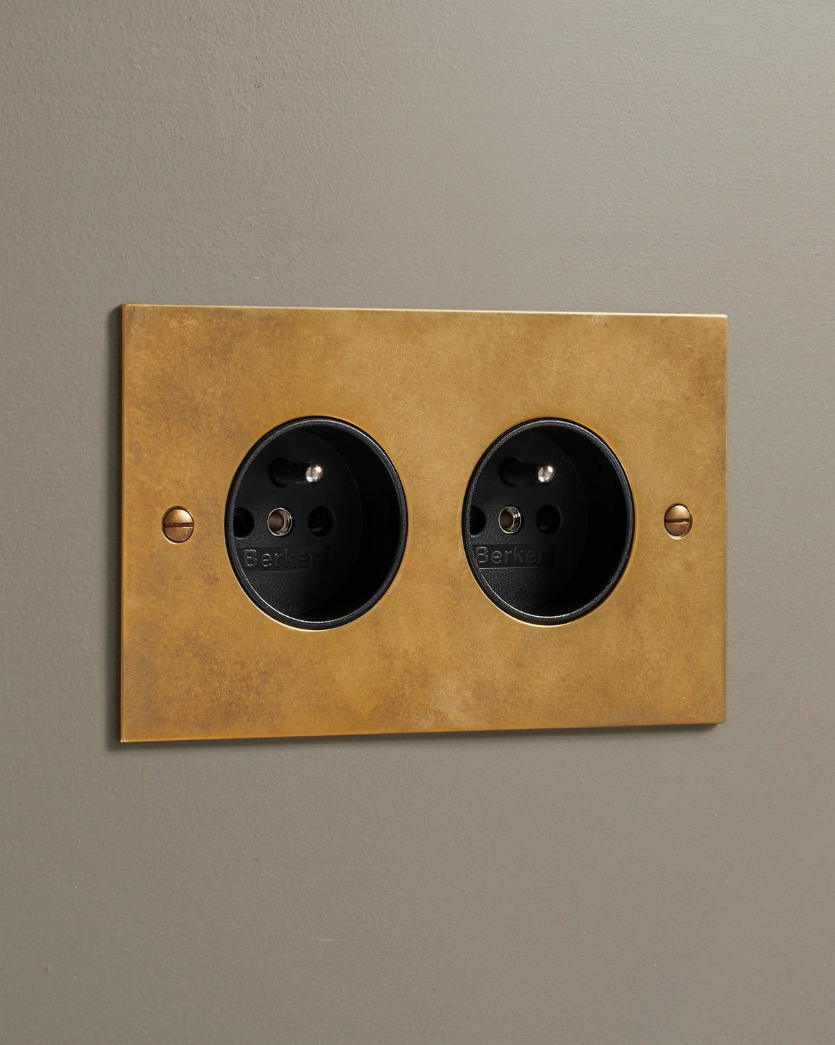 An oblique view of a classic French-style twin plug socket in a warm burnished brass finish. TEST