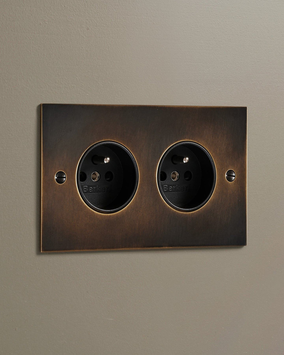 An oblique view of a classic French-style twin plug socket in a dark oxidised brass finish. TEST