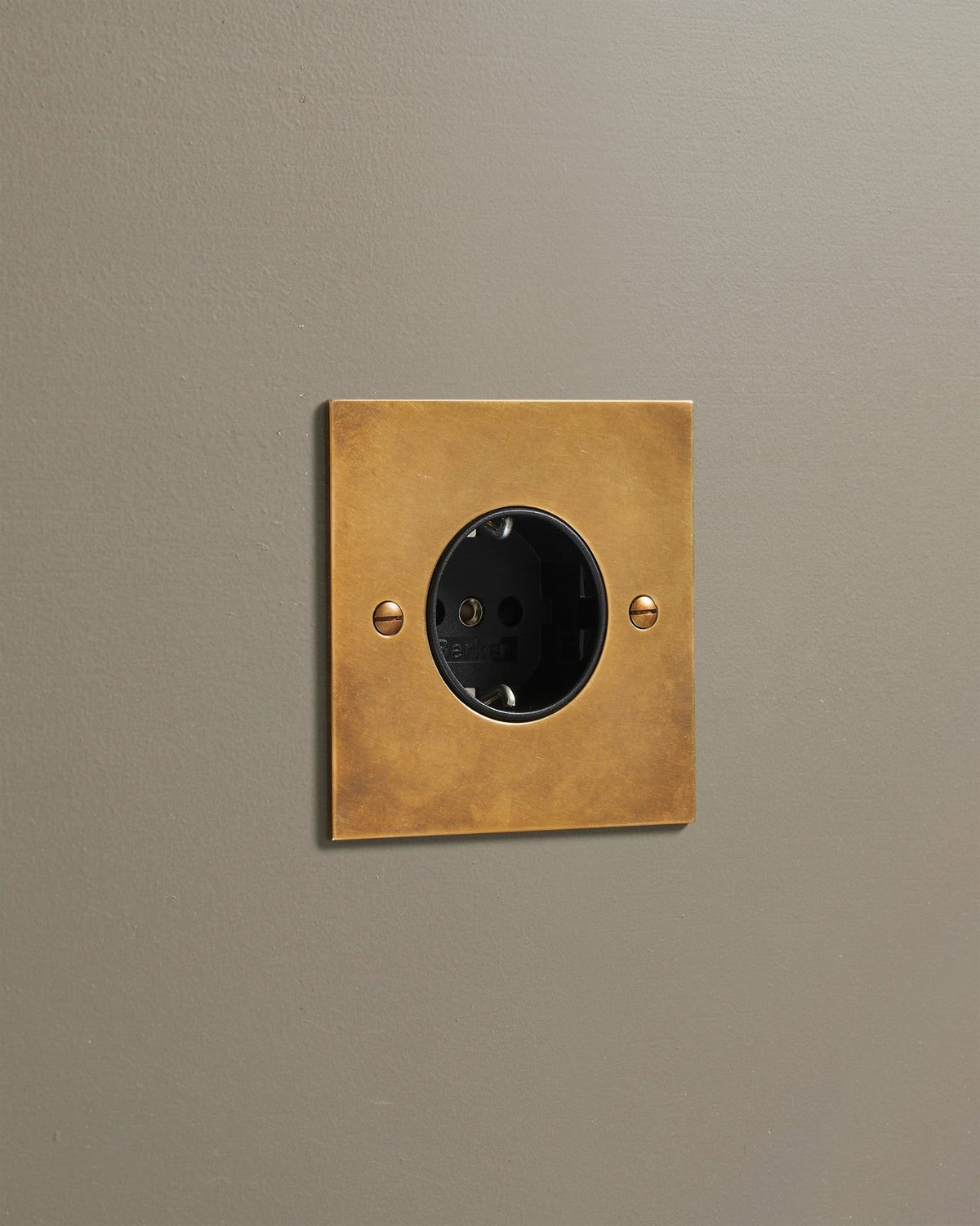 An oblique view of a classic Schuko-style single plug socket in a warm burnished brass finish. TEST