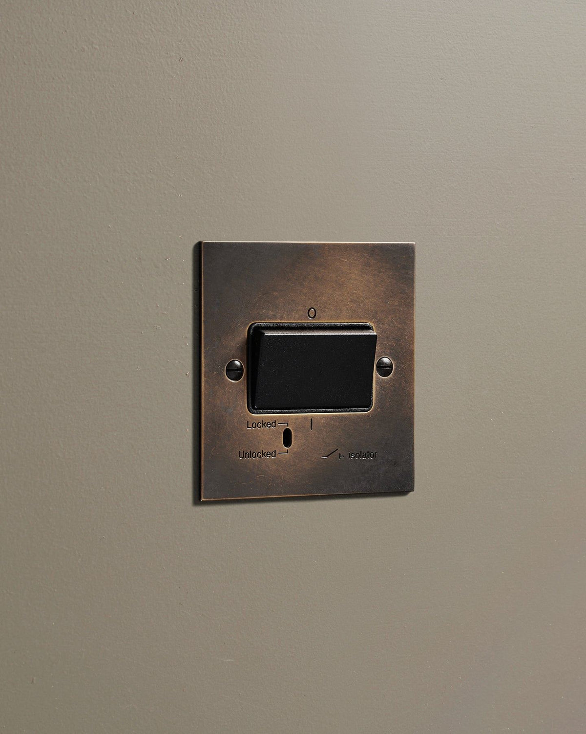 An oblique view of a classic extractor fan isolator switch in a dark oxidised brass finish. TEST