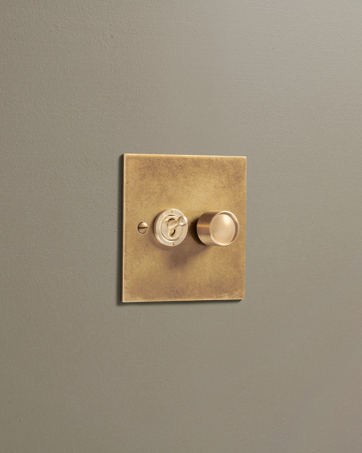 An oblique view of a 2 gang classic toggle and dimmer mixed switch in a mottled aged brass finish. TEST
