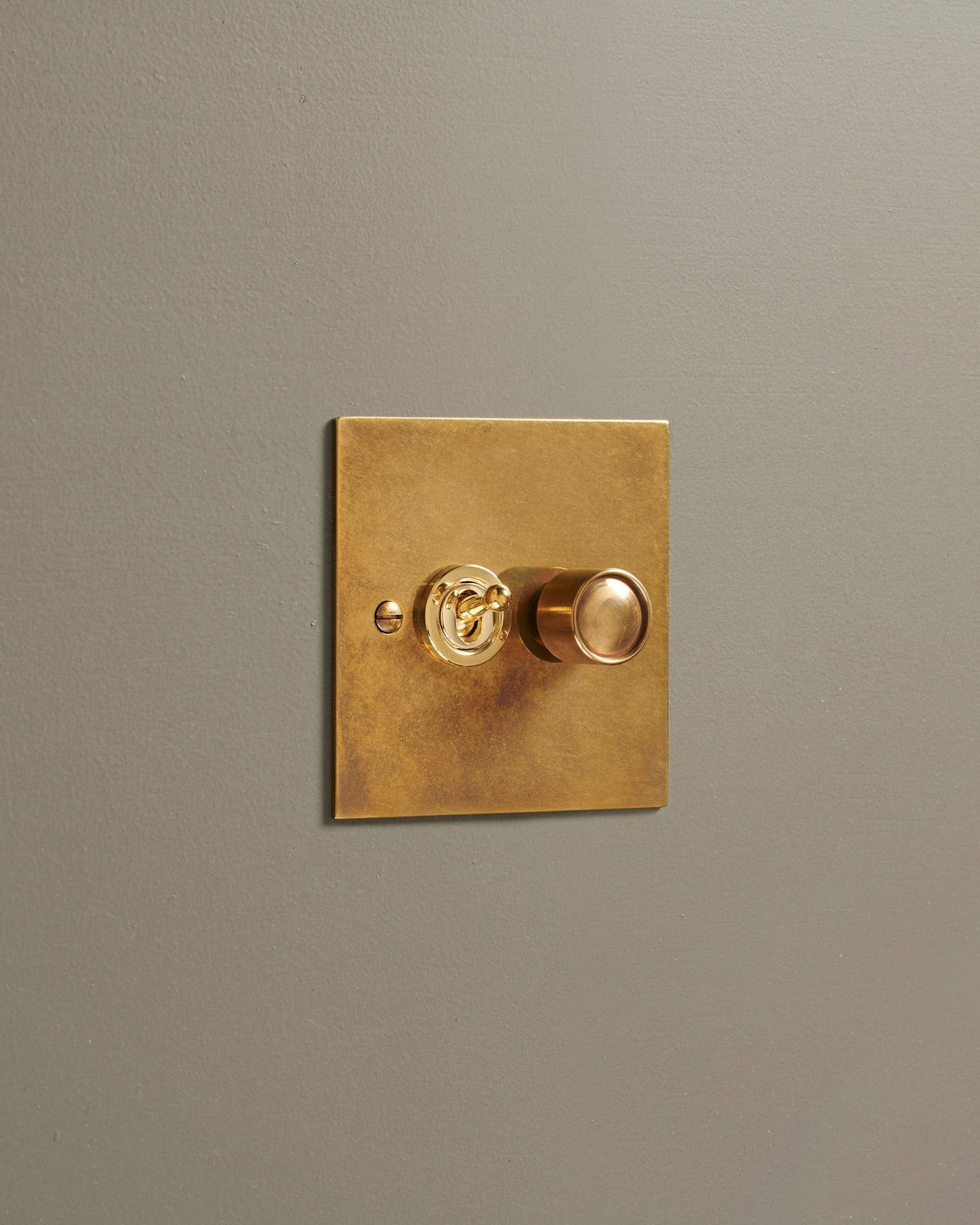 An oblique view of a 2 gang classic toggle and dimmer mixed switch in a warm burnished brass finish. TEST