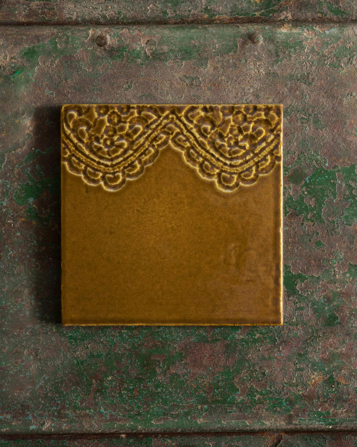 Decorative sepia tile with lace pattern on a textured green surface. | Florentine Scallop Square TEST