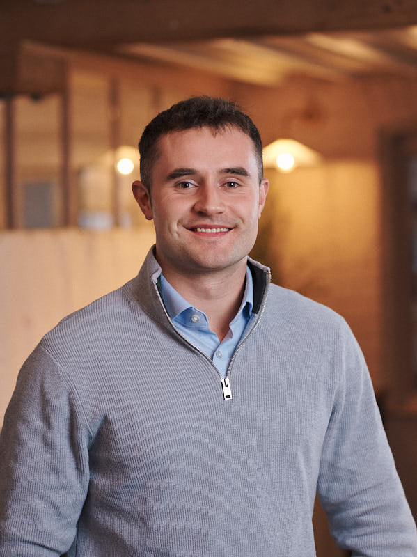 Man wearing a gray sweater over a blue shirt in an indoor setting