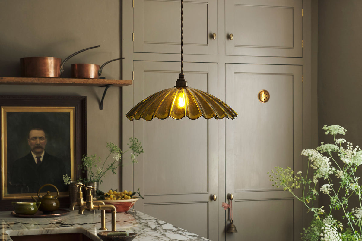 A large chartreuse frilly glass light hanging in a moody grey kitchen.