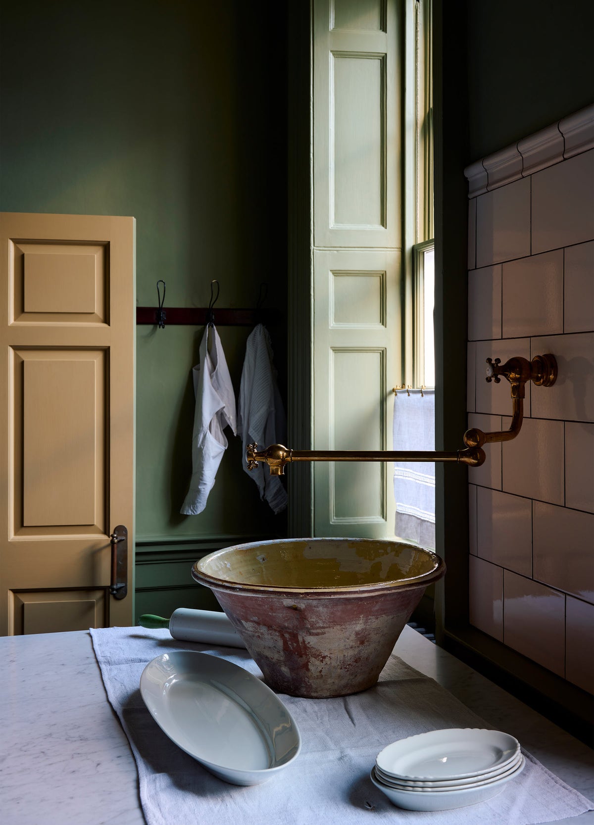 An oblique view of a traditional-style aged brass pot filler tap in a dark Georgian-style kitchen, the tap is fully extended above a large ceramic bowl on the worktop below.