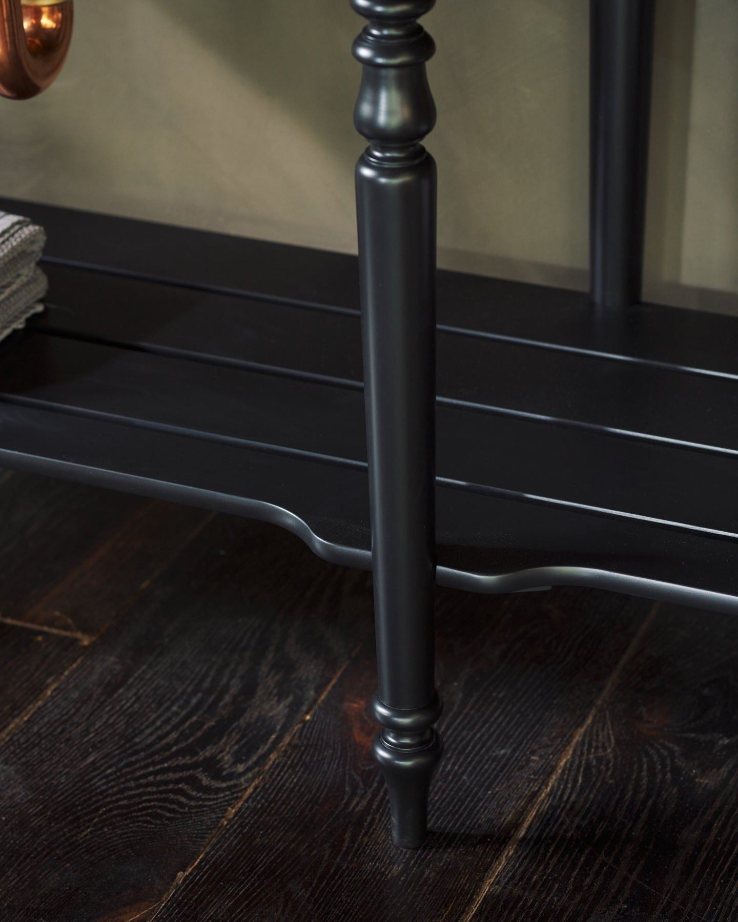 A close-up view of a black painted slatted shelf at the base of a Victorian-inspired washstand.