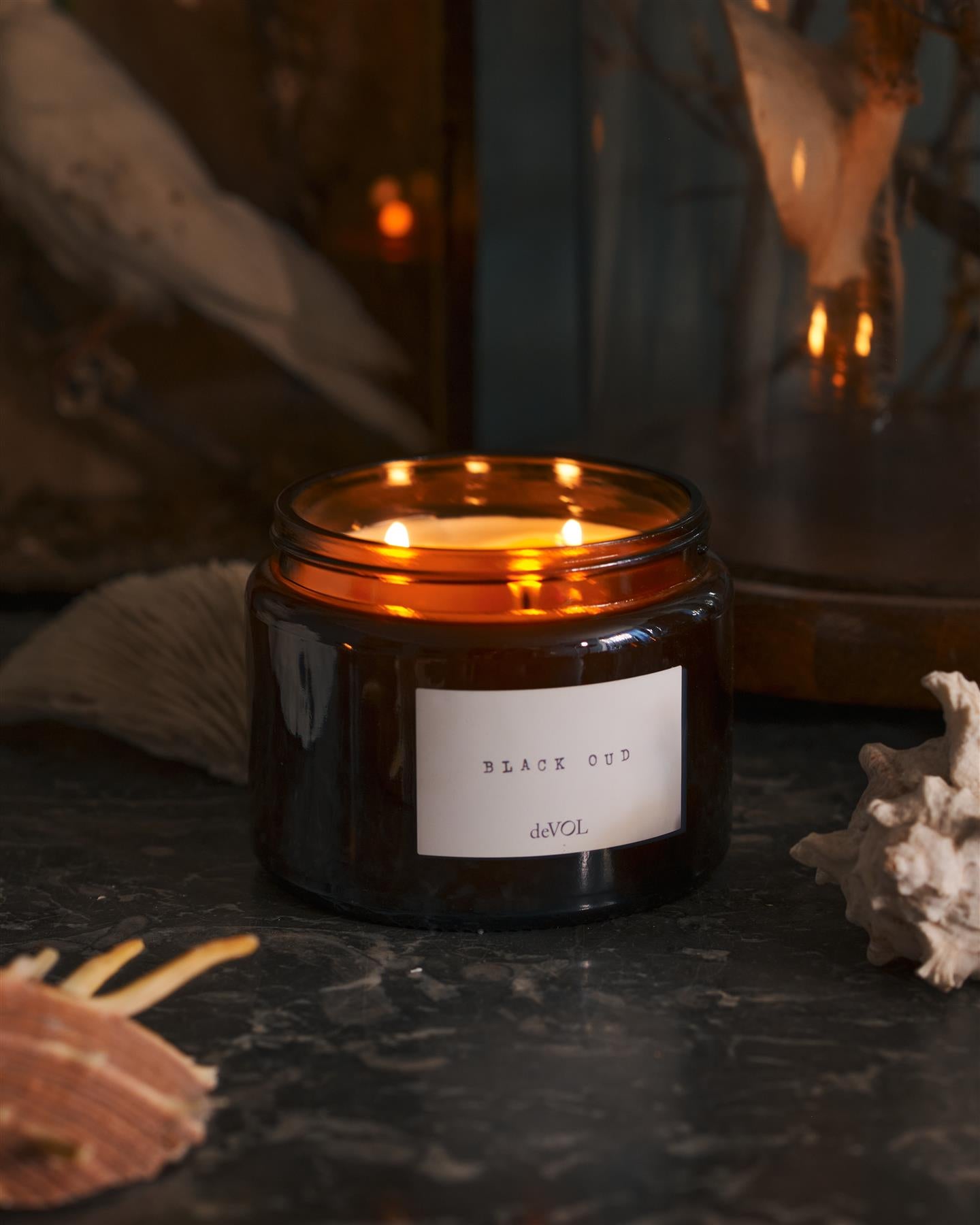 A lit large scented candle in a brown glass jar with three wicks, on a polished quartz worktop.