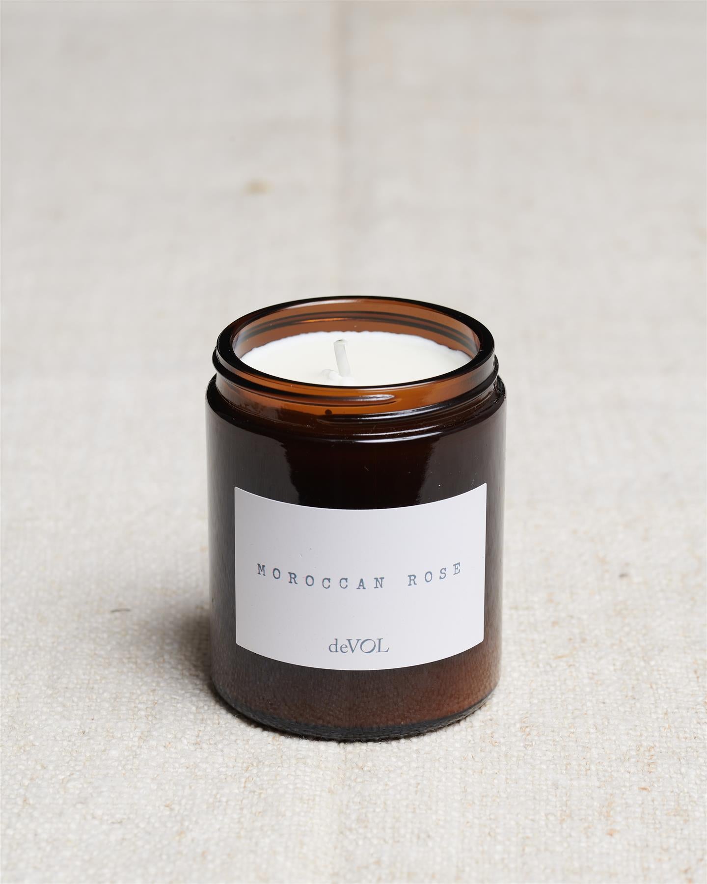 A collection of three lit scented candles in brown glass jars on a polished quartz worktop; small, medium and large.