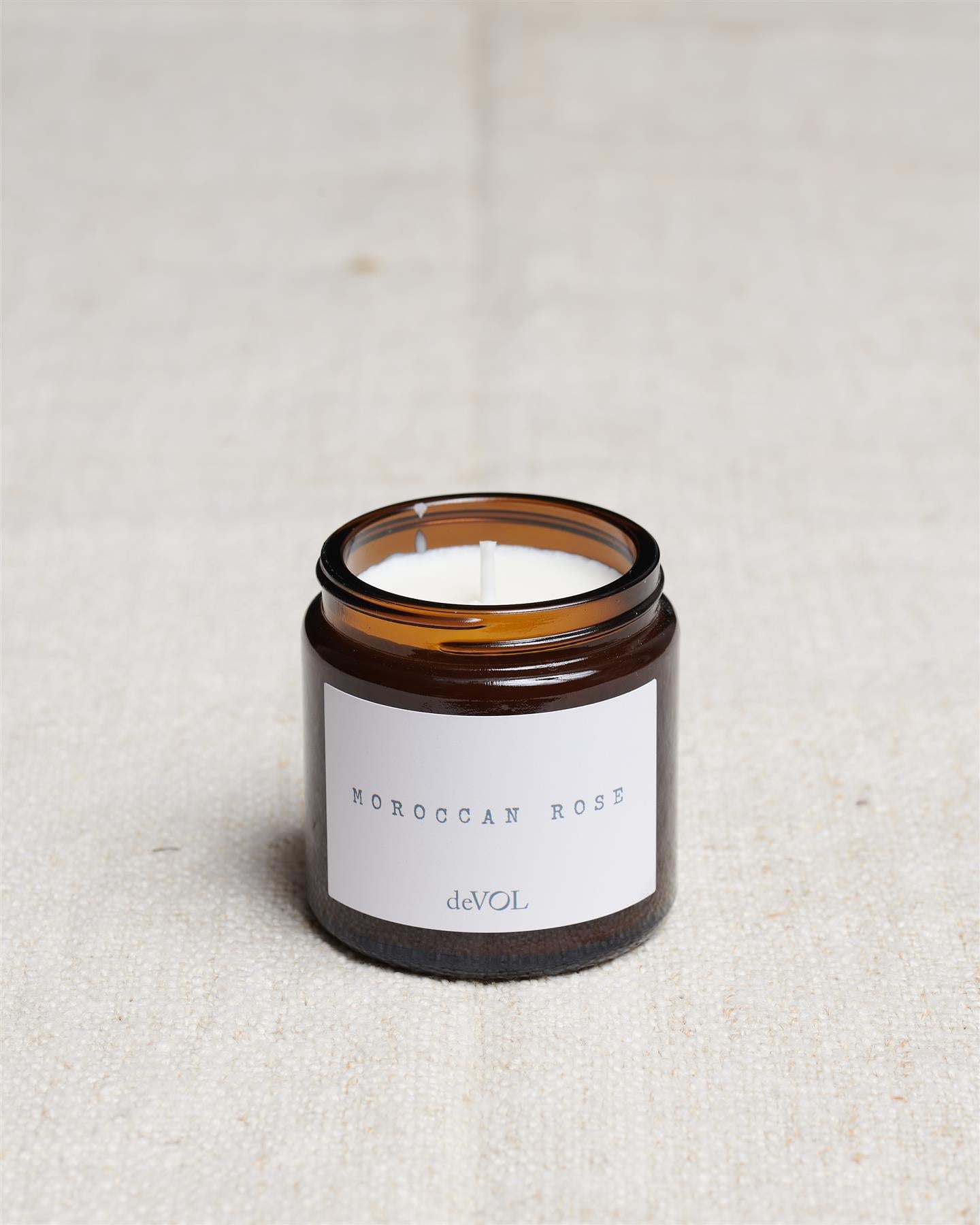 A collection of three lit scented candles in brown glass jars on a polished quartz worktop; small, medium and large.