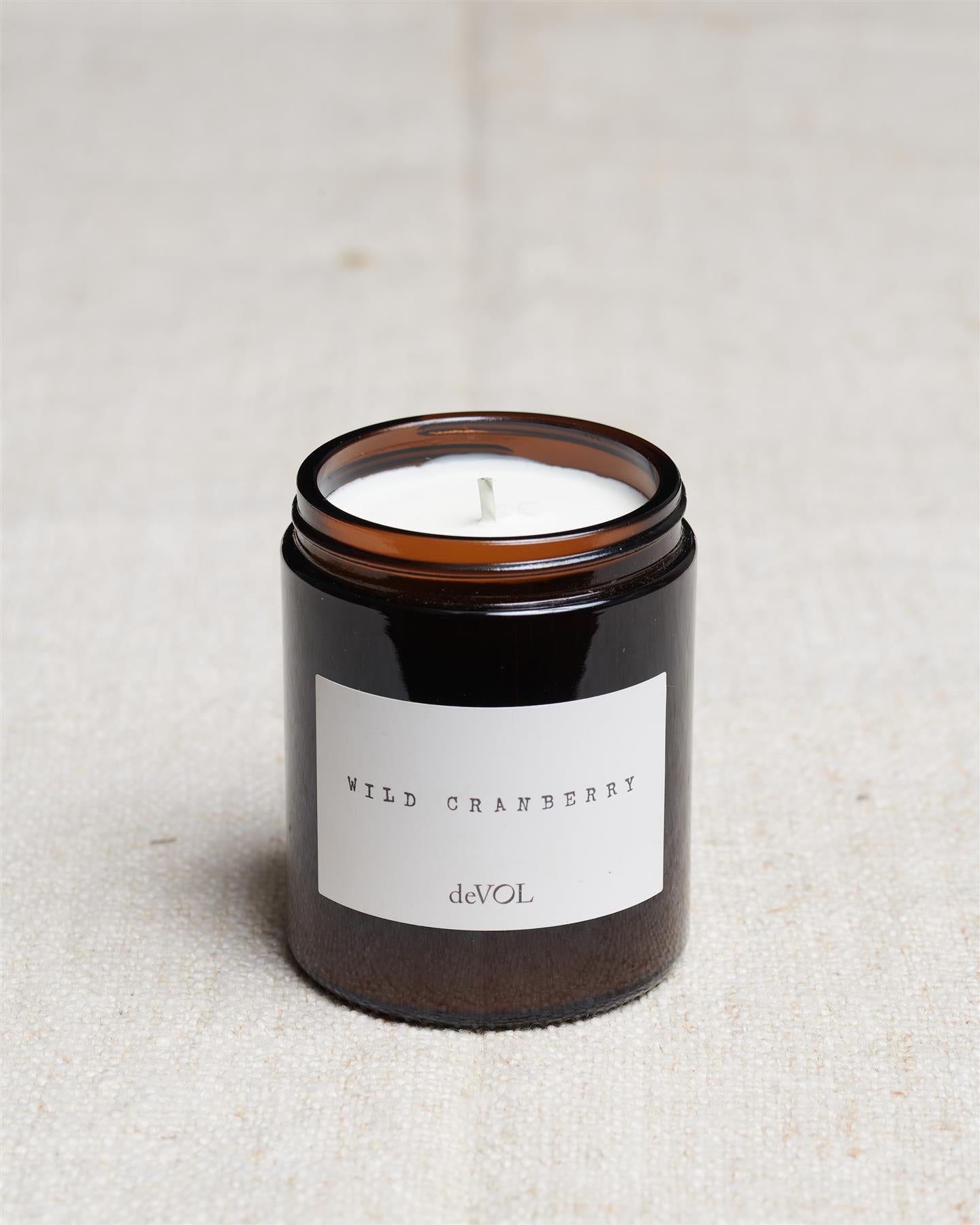 A collection of three lit scented candles in brown glass jars on a polished quartz worktop; small, medium and large.