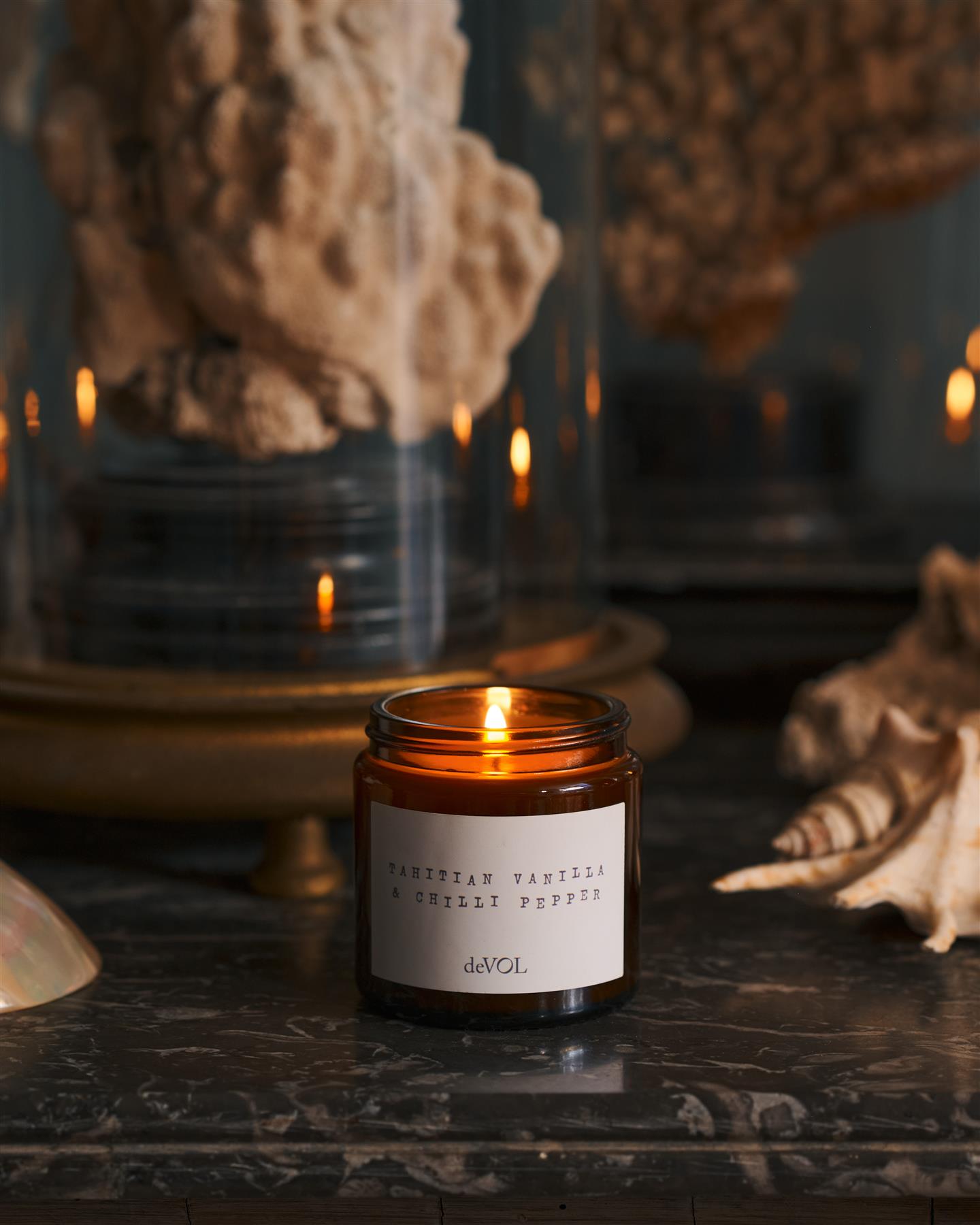 A collection of three lit scented candles in brown glass jars on a polished quartz worktop; small, medium and large.