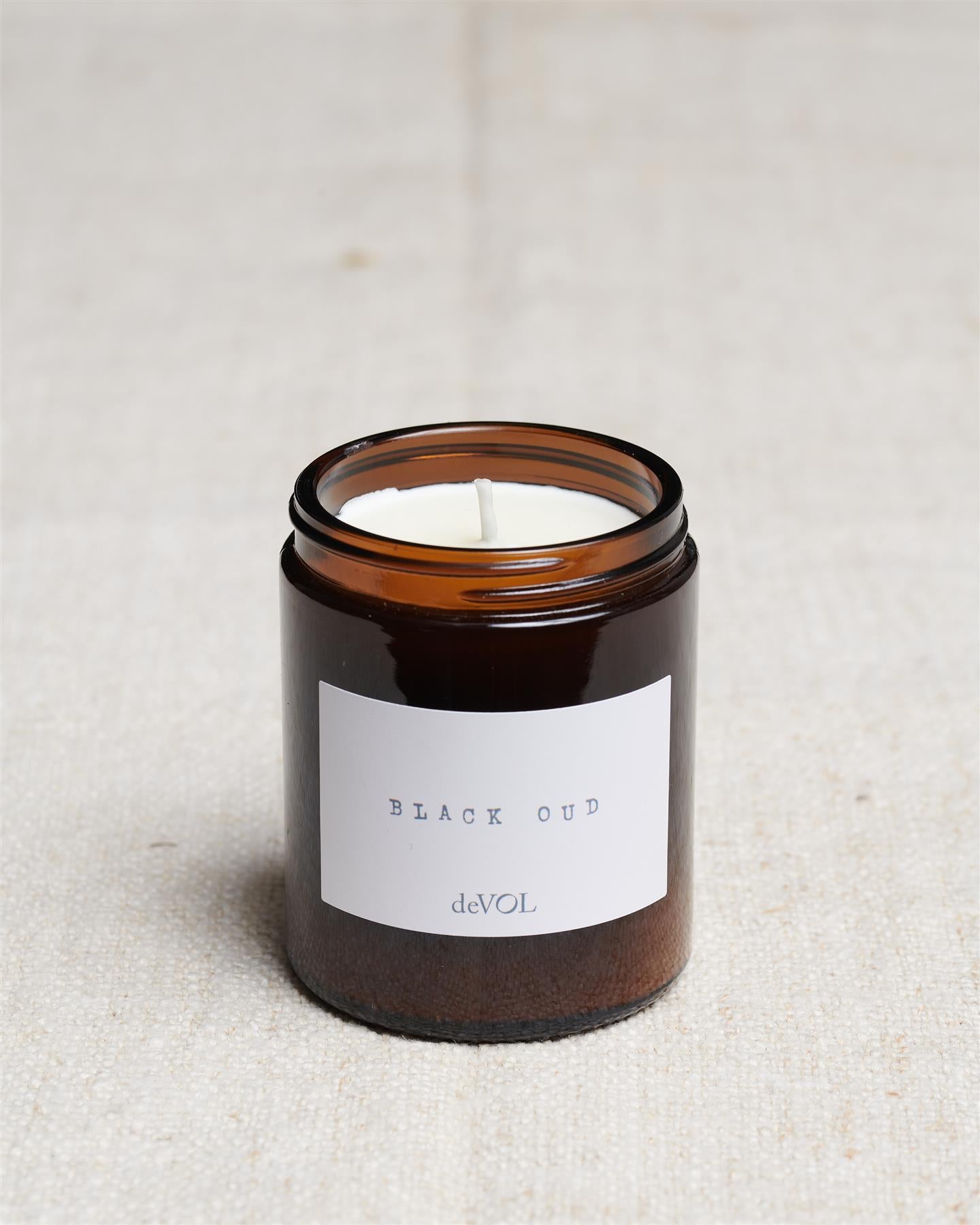 A collection of three lit scented candles in brown glass jars on a polished quartz worktop; small, medium and large.