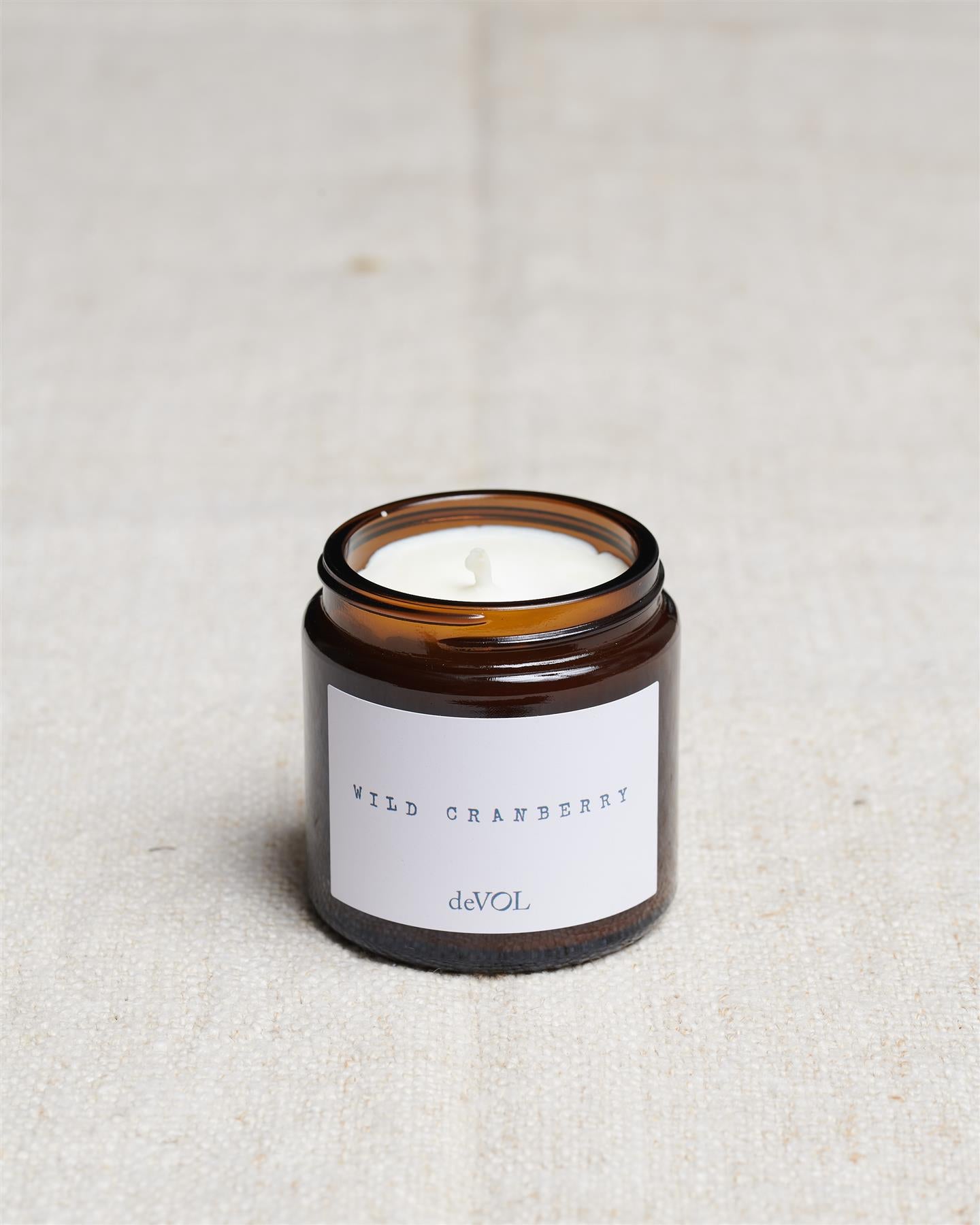 A collection of three lit scented candles in brown glass jars on a polished quartz worktop; small, medium and large.