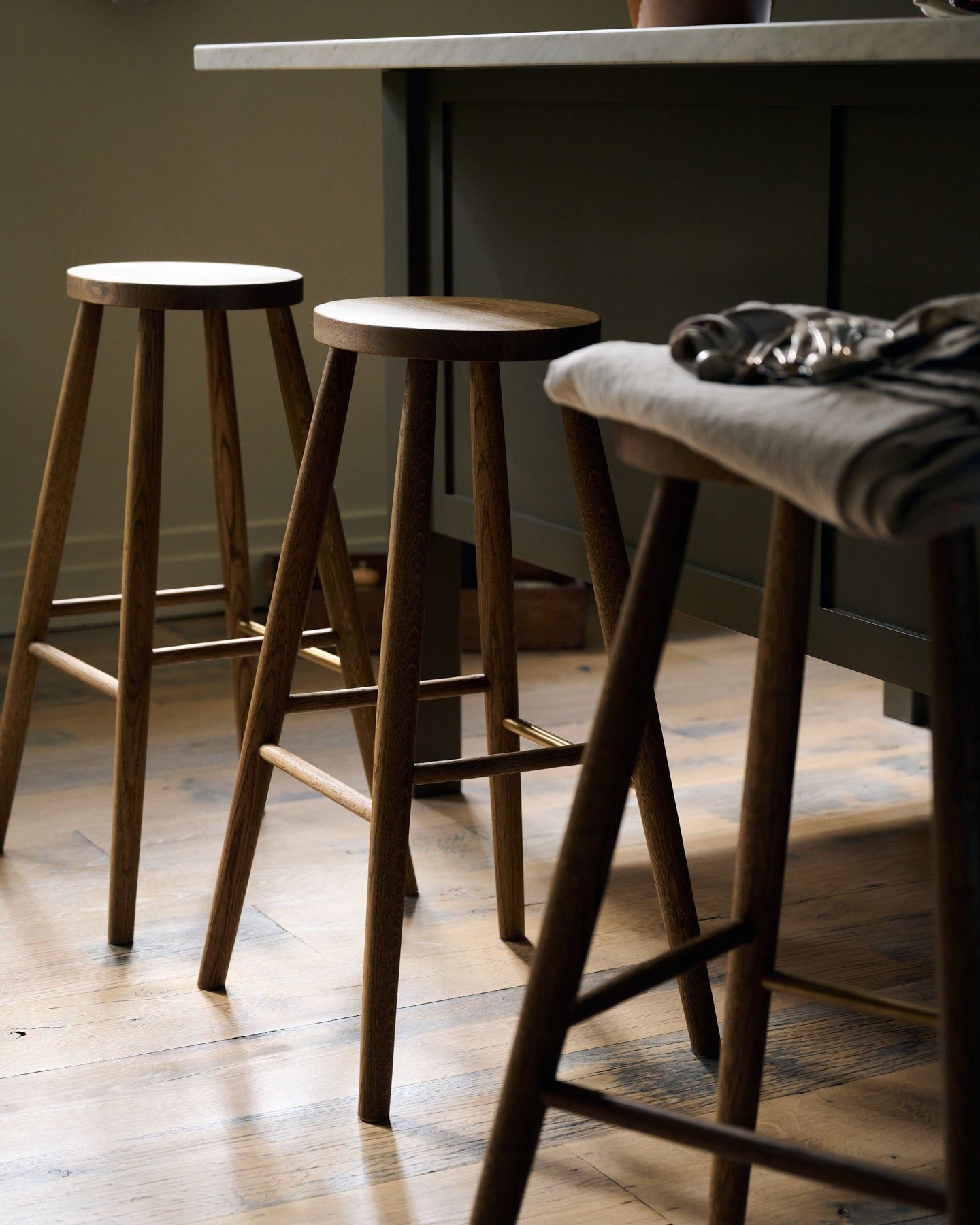 An oblique view of threee simple oak bar stools with oval-shaped seats in front of an island breakfast bar.