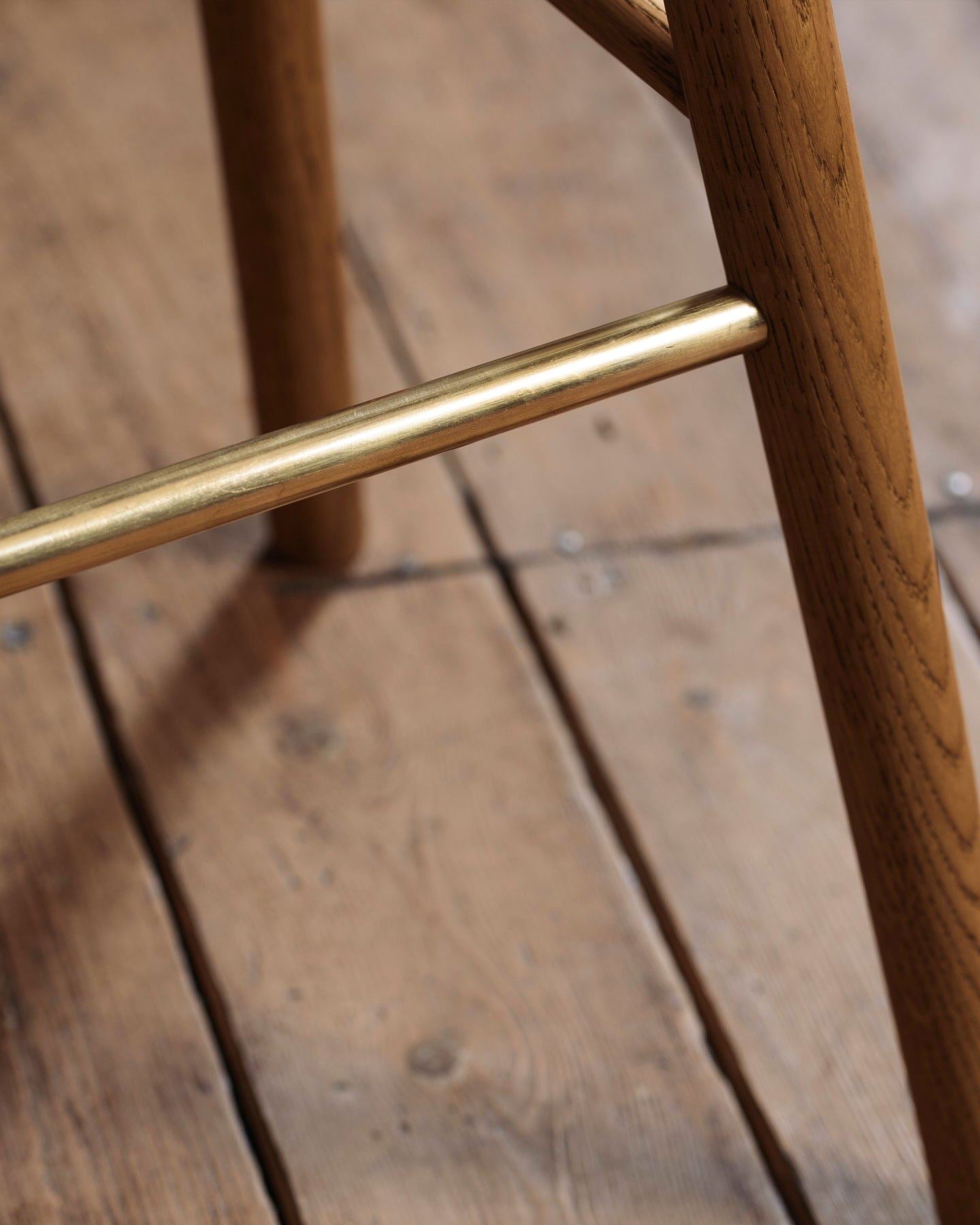 A close-up view of a brass footrail from an oak bar stool.