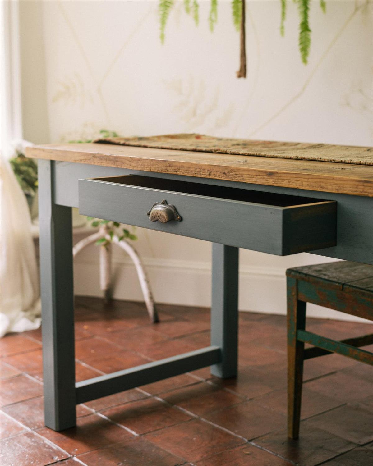 An oblique view of a shallow drawer with a bohemian-style brass handle from a banquet-style dining table. TEST