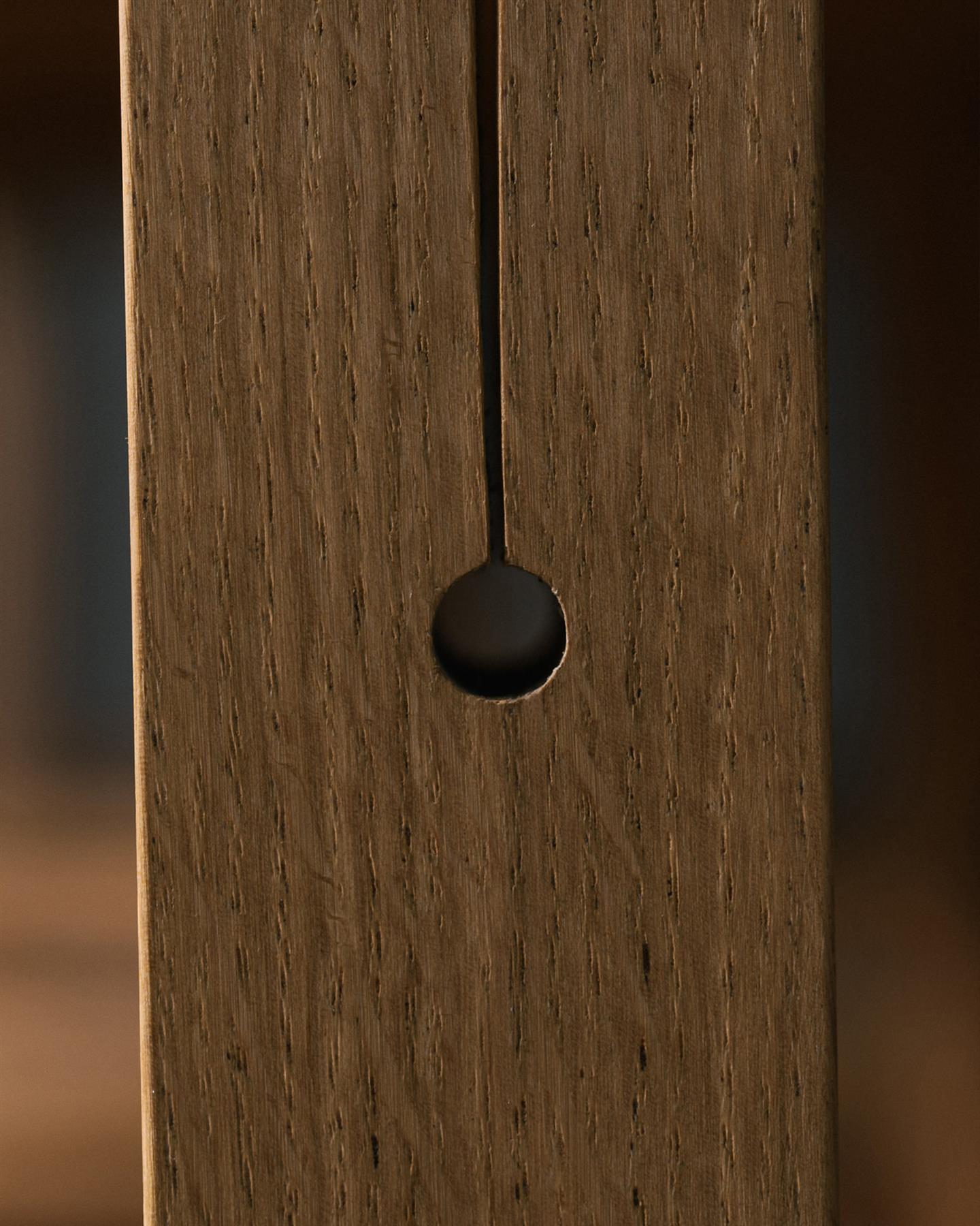 A close-up view of a circular hole at the base of a split design in an oak table leg.