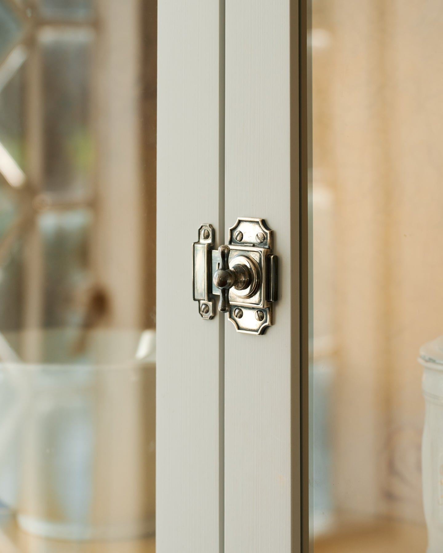 A close-up oblique view of a Victorian-inspired rack and pinion cupboard catch in a tarnished silver finish fitted to white painted doors.