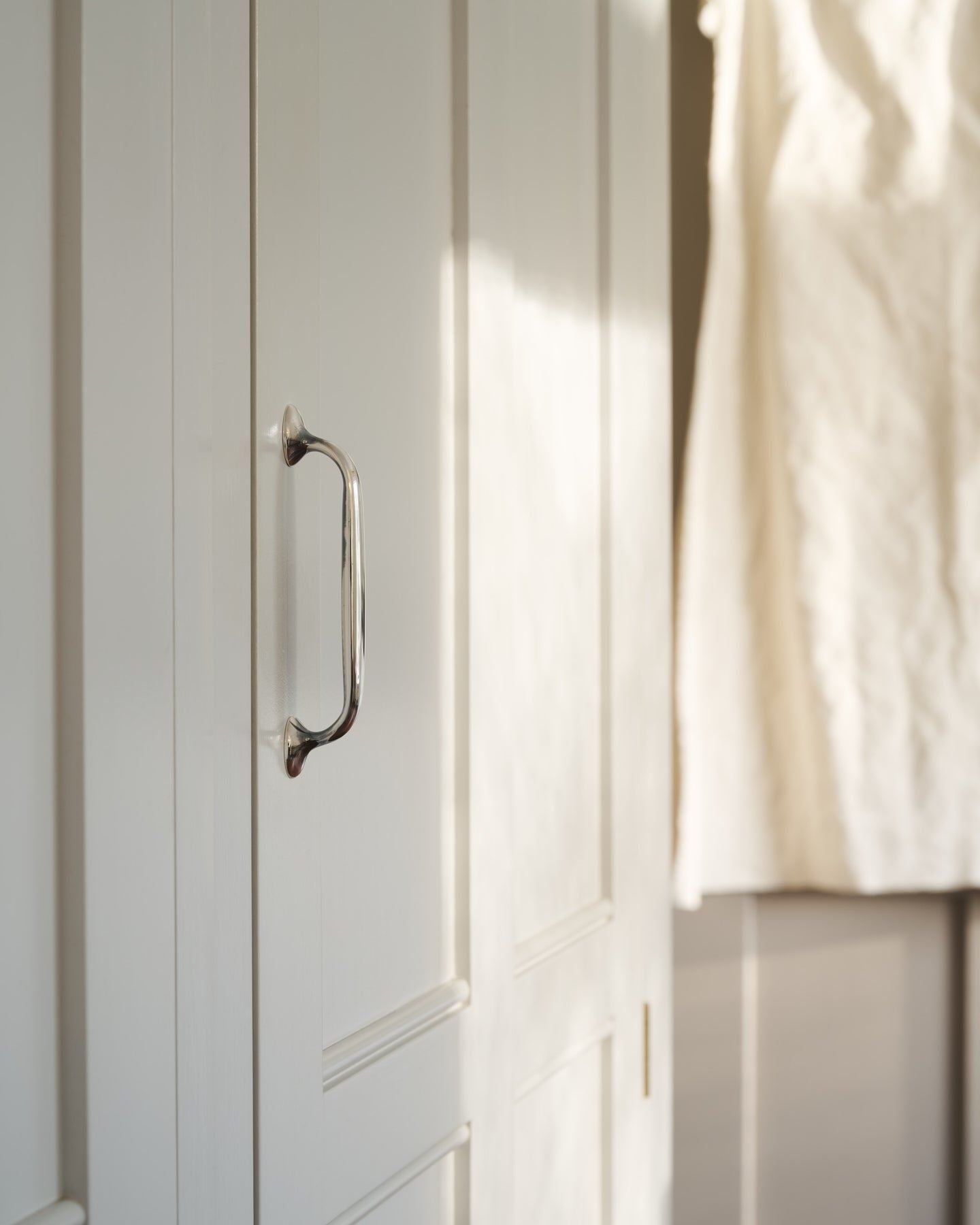 An oblique view of a white painted Georgian-style pantry cupboard with a simple pull handle in a tarnished 'Bella' silver finish.