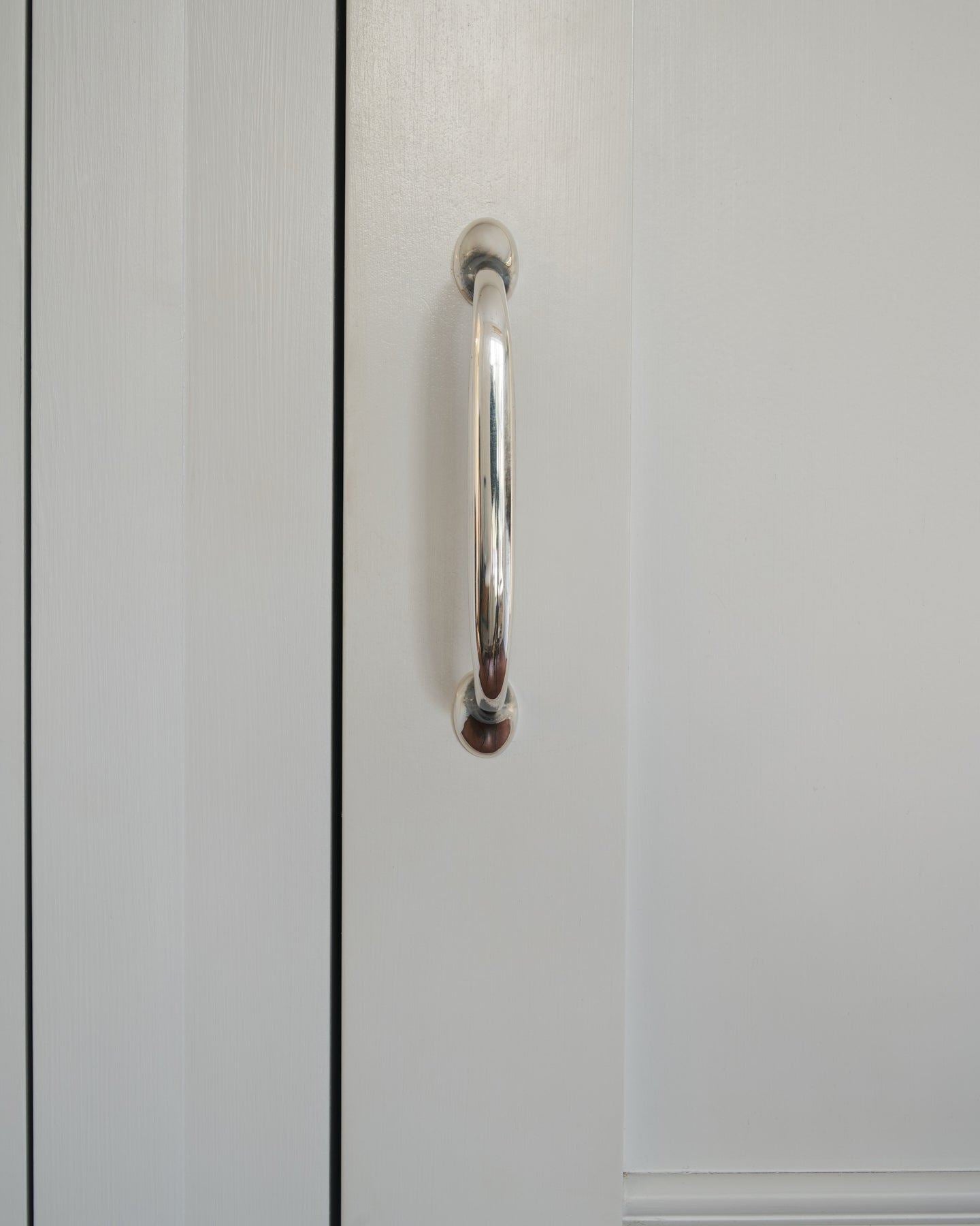 A close-up straight-on view of a simple pull handle in a tarnished 'Bella' silver finish, fitted to a white painted door.
