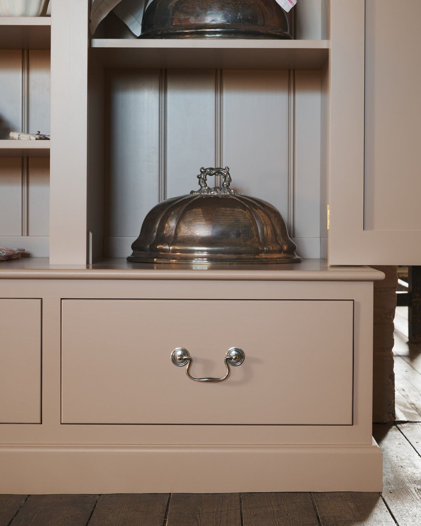 A close-up straight-on view of a dusty pink painted pantry cupboard with bottom drawers, fitted with Georgian-style cup handles in a tarnished 'Bella' silver finish.