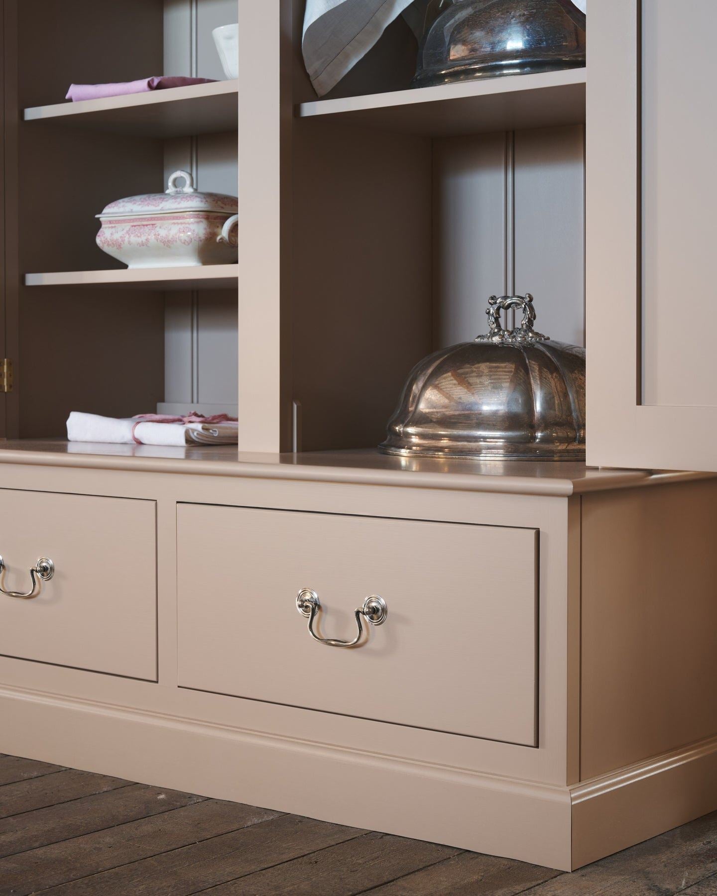 An oblique view of a dusty pink painted pantry cupboard with bottom drawers, fitted with Georgian-style cup handles in a tarnished 'Bella' silver finish.
