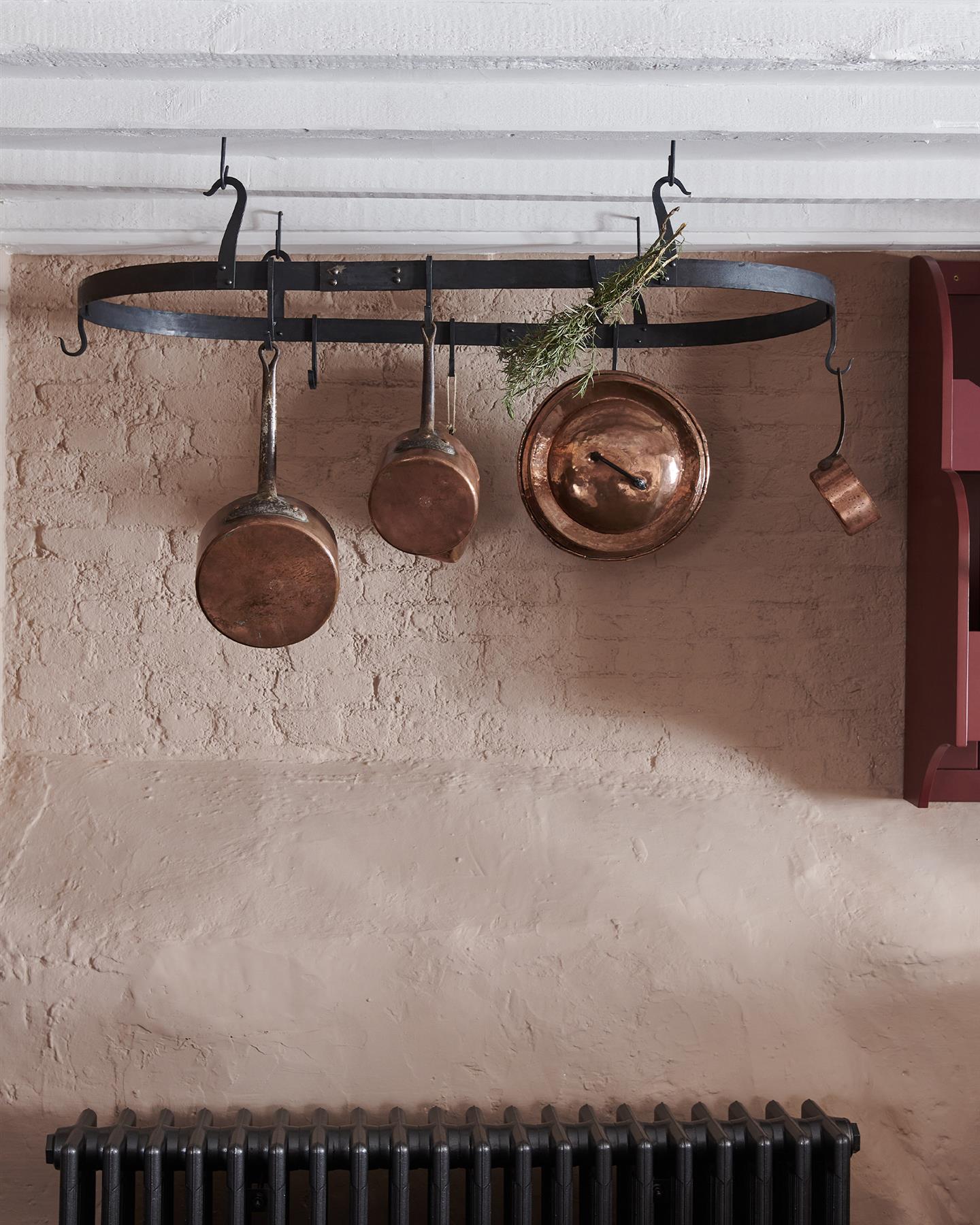 A straight-on view of a large oval-shaped wrought iron pot hanger suspended from a beamed ceiling via iron hooks.