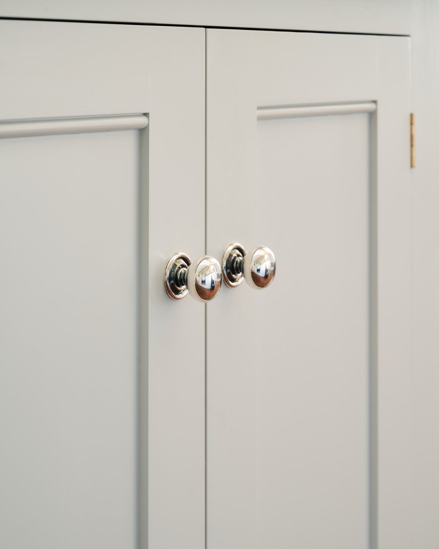 An oblique view of a pair of round doorknobs with pressed backplates in a tarnished silver finish, fitted to white painted Georgian-style kitchen cupboard doors.