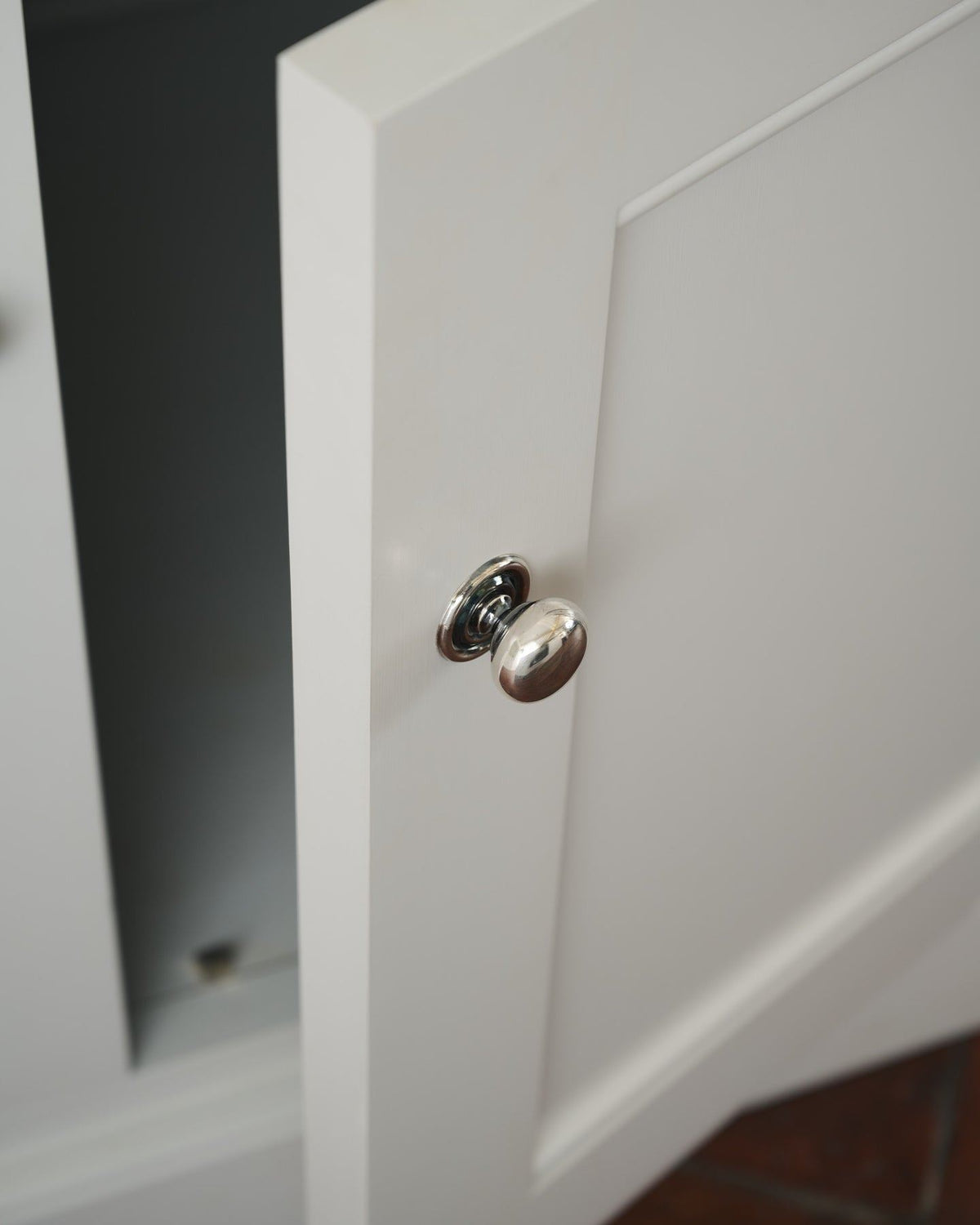 A round doorknob with a pressed backplate in a tarnished silver finish, fitted to an open white painted kitchen cupboard door.| Small shown TEST