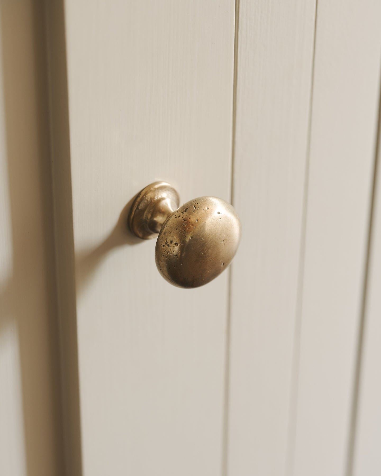 A close-up oblique view of a classic knob in an aged brass finish, fitted to a mushroom painted cupboard door.