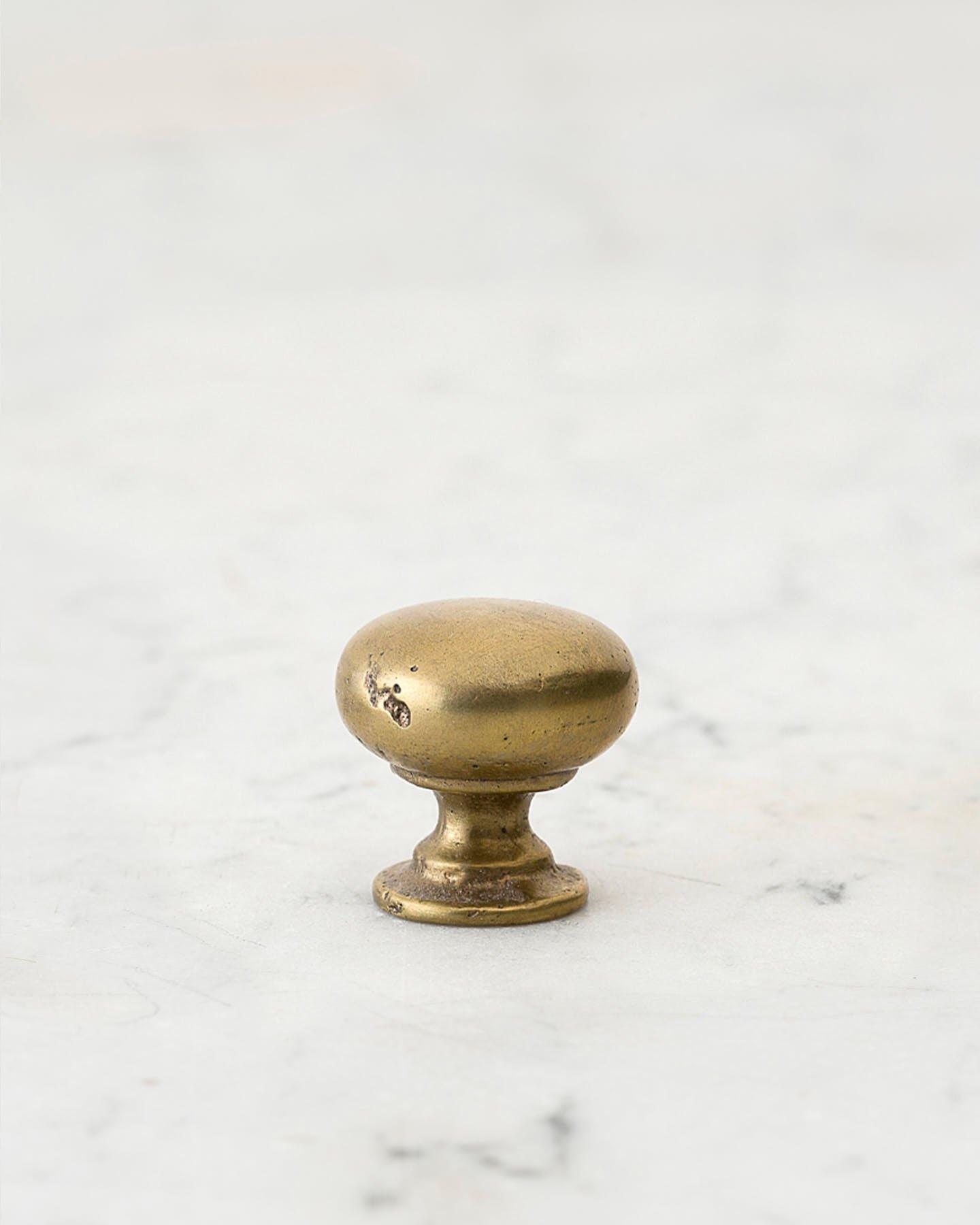 A 'Large' classic knob for a kitchen cupboard or drawer with an aged brass finish and unique dented textures that makes it look like a beloved, well aged brass from centuries ago.