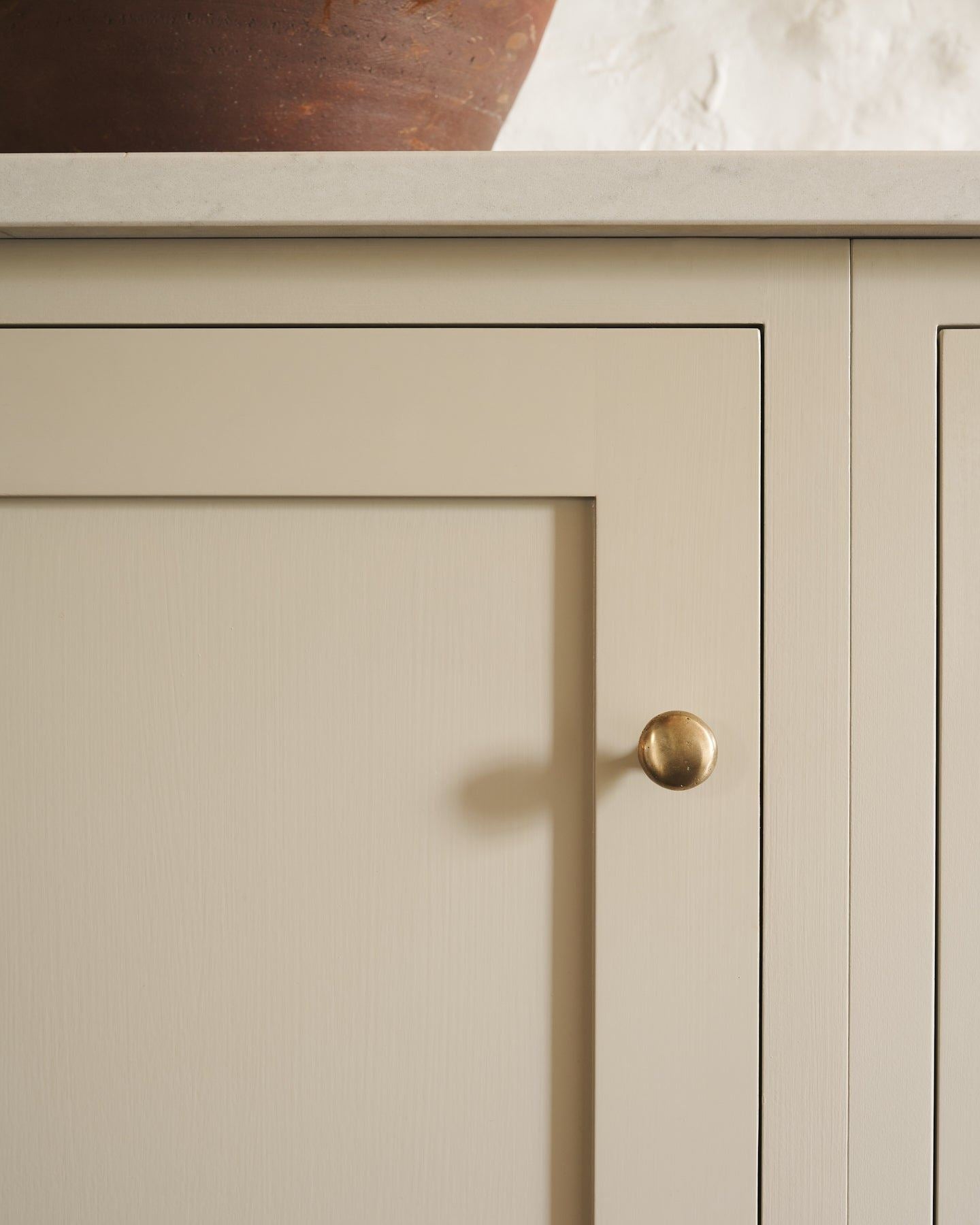 A straight-on view of a classic knob in an aged brass finish, fitted to a mushroom painted cupboard door.