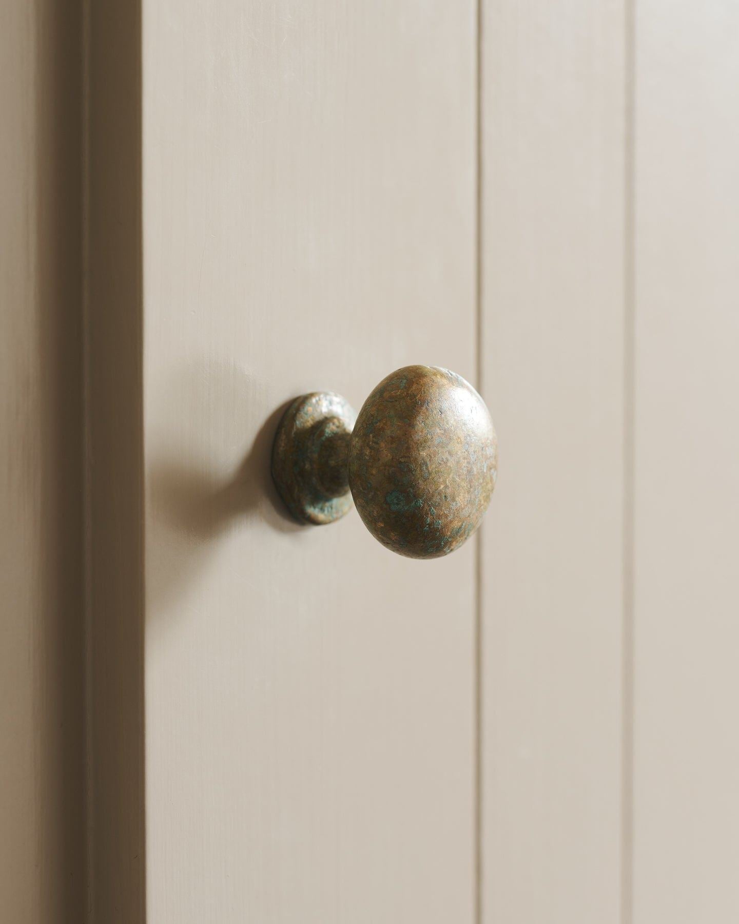 A close-up oblique view of a classic knob in an aged verdrigris brass finish, fitted to a mushroom painted cupboard door.