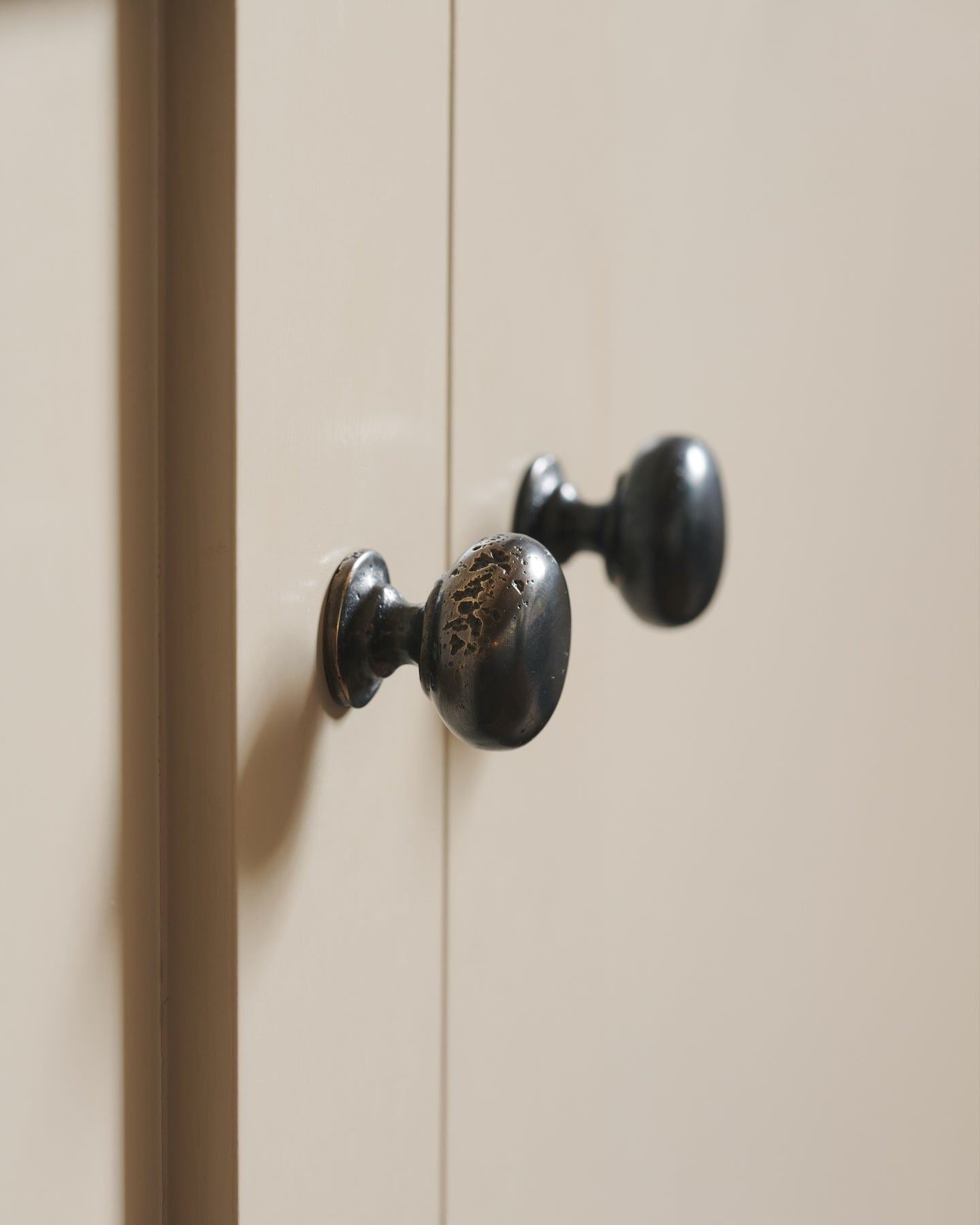 A close-up profile view of a pair of classic knobs in a dark oxidised bronze finish, fitted to a mushroom painted Shaker-style kitchen cupboard.