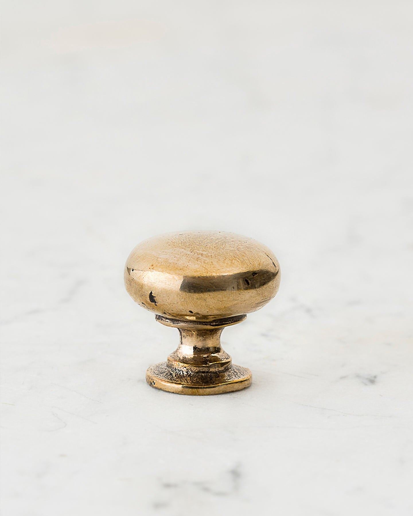 A 'Small' classic knob for a kitchen cupboard or drawer with a bright polished bronze finish and unique dented textures that makes it look like a beloved, well aged bronze from centuries ago.