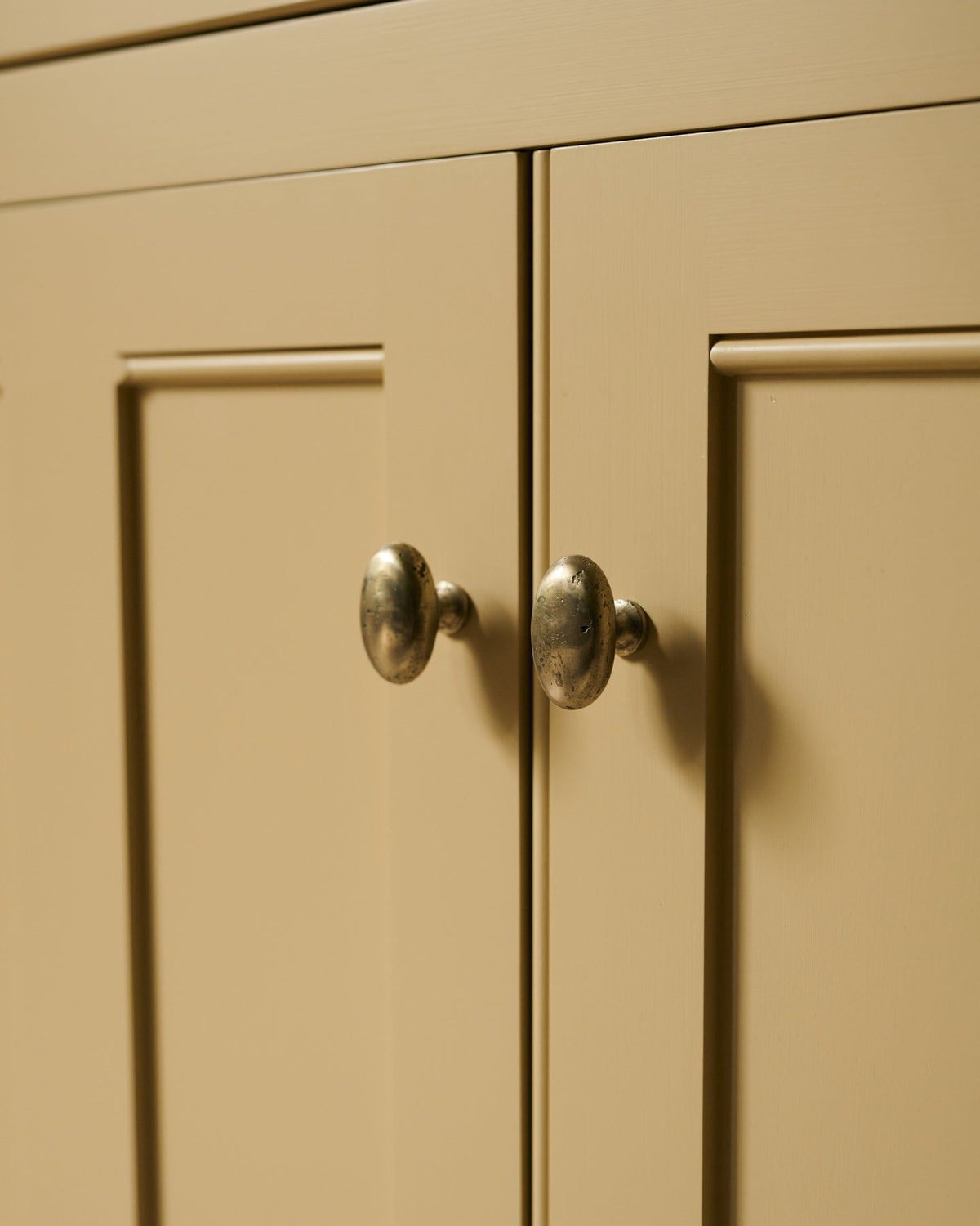An oblique view of a pair of oval-shaped knobs in an aged brass finish, fitted to a yellow painted Georgian-style kitchen cupboard.|Aged Brass Large shown TEST