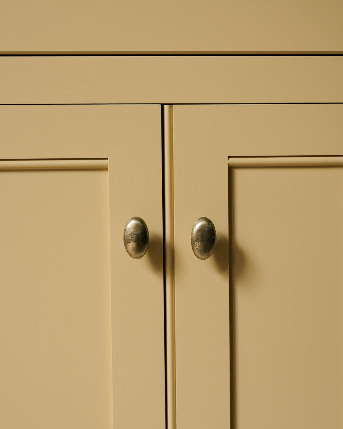 A straight-on view of a pair of oval-shaped knobs in an aged brass finish, fitted to a yellow painted Georgian-style kitchen cupboard.|Aged Brass Large shown TEST