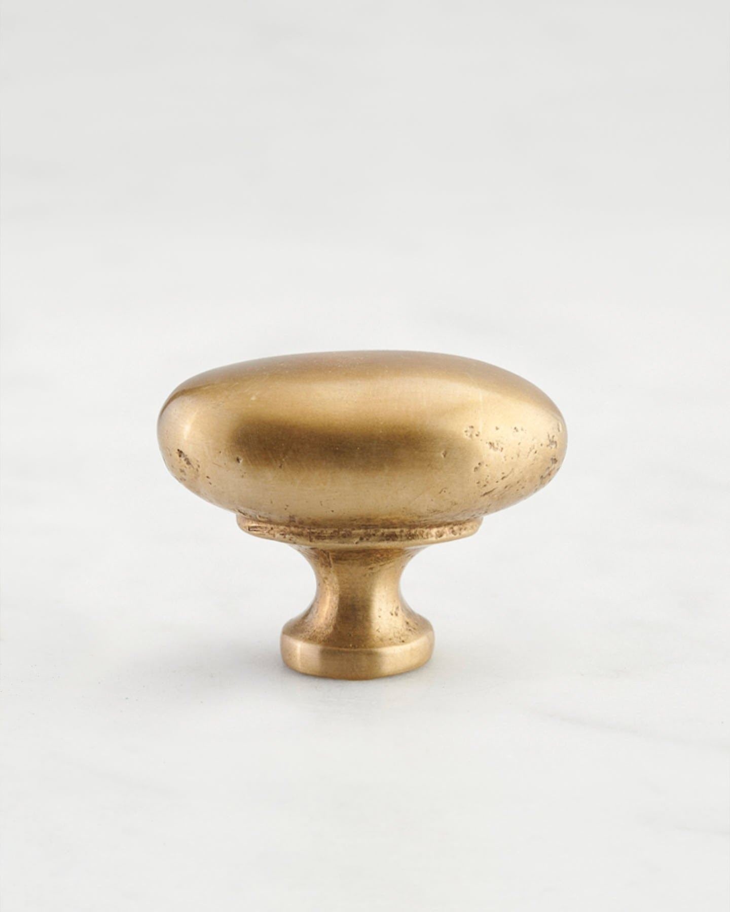 A 'Medium' oval-shaped knob for a kitchen cupboard or drawer with an aged brass finish and unique dented textures that makes it look like a beloved, well aged brass from centuries ago.