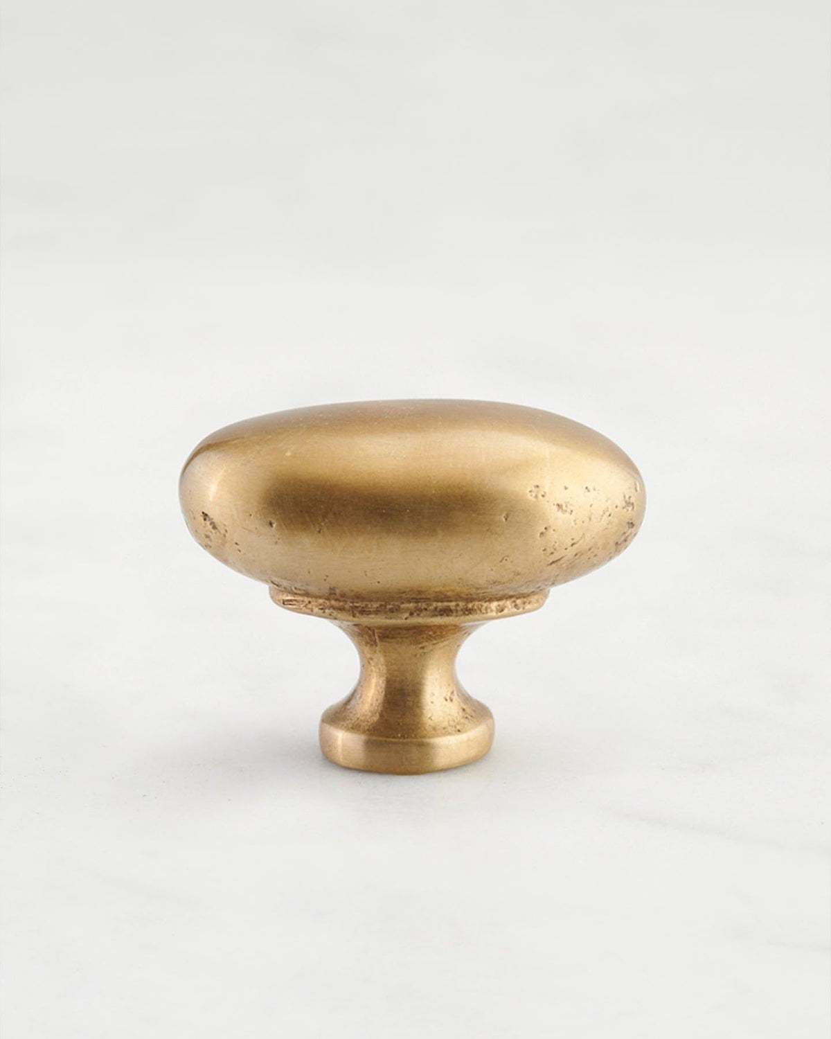 A 'Medium' oval-shaped knob for a kitchen cupboard or drawer with an aged brass finish and unique dented textures that makes it look like a beloved, well aged brass from centuries ago. TEST