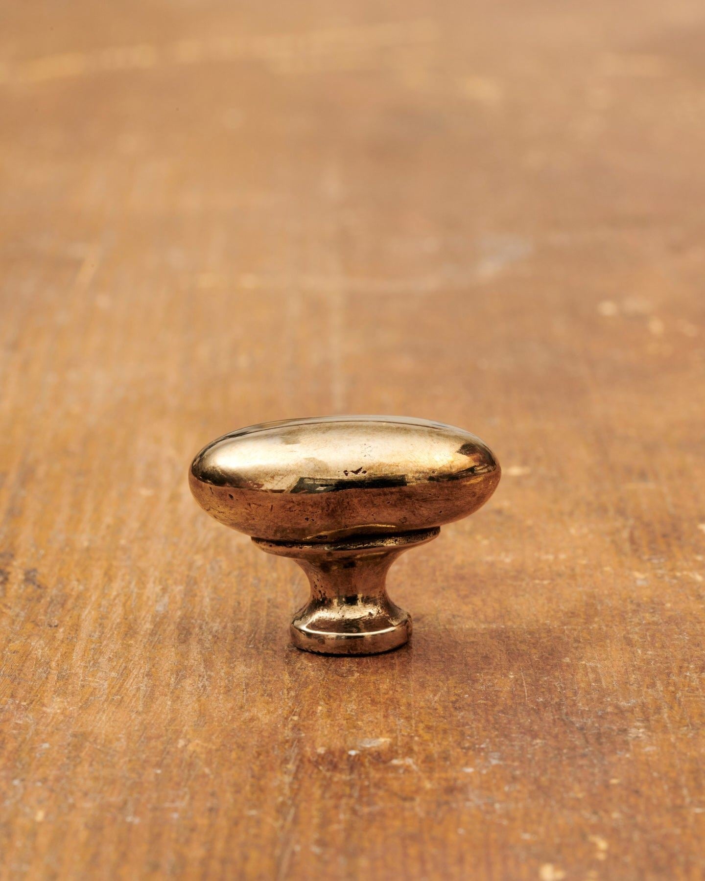A 'Small' oval-shaped knob for a kitchen cupboard or drawer with a warm burnished brass finish and unique dented textures as if was made by an artisan blacksmith centuries ago.