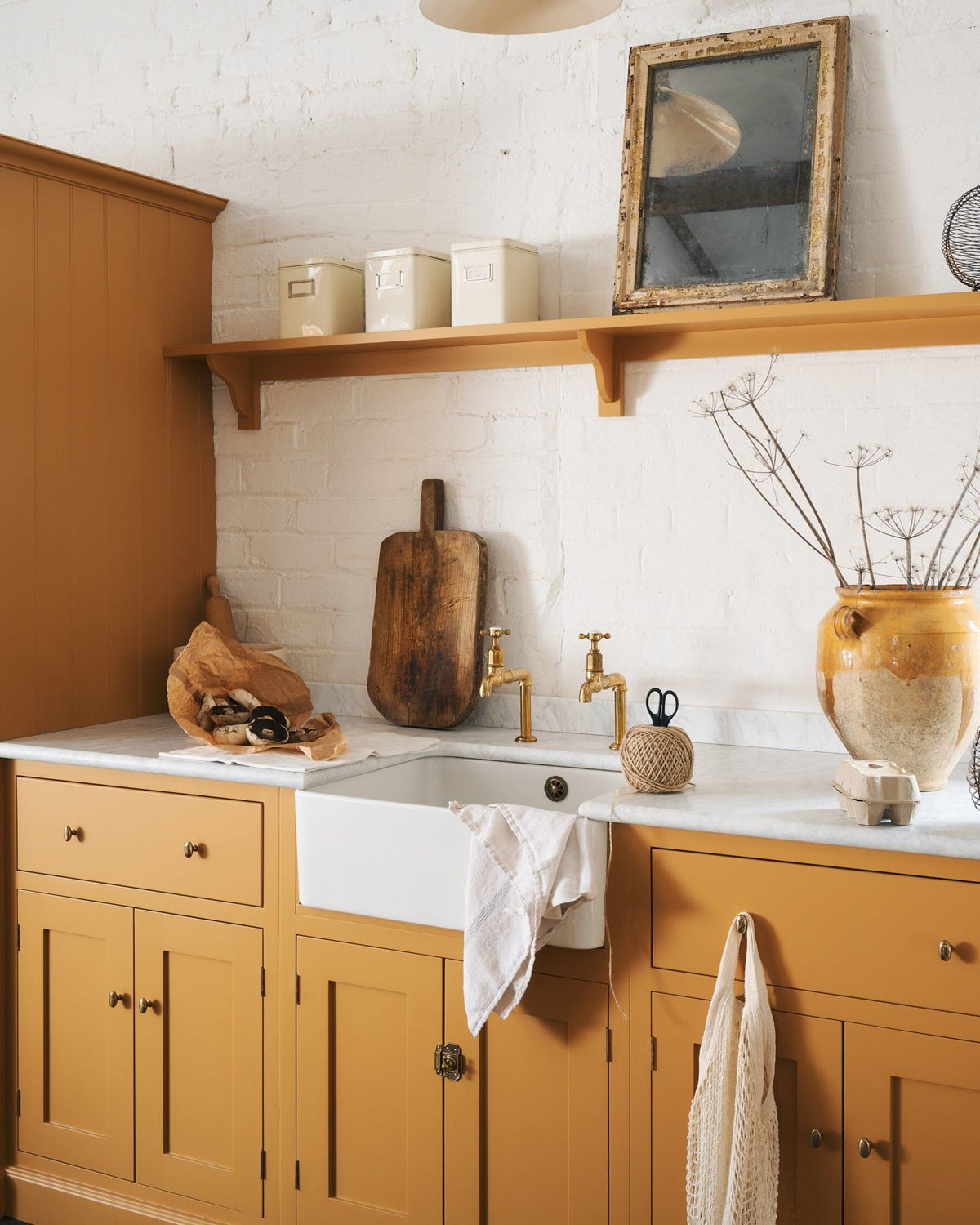 An oblique view of a yellow painted Shaker-style kitchen sink cupboard with small oval-shaped knobs in a warm burnished brass finish.|Small shown TEST