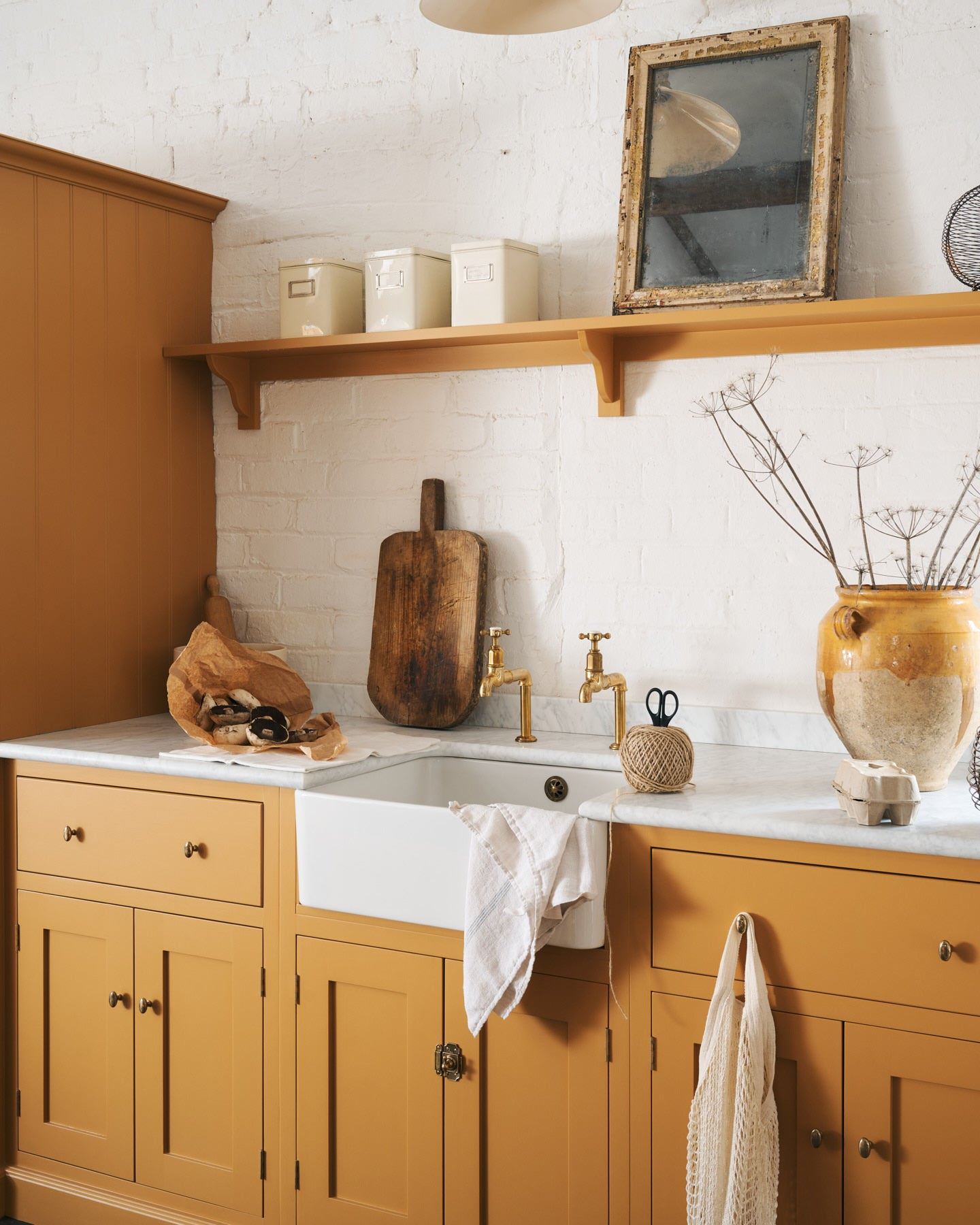 An oblique view of a yellow painted Shaker-style kitchen sink cupboard with small oval-shaped knobs in a warm burnished brass finish.