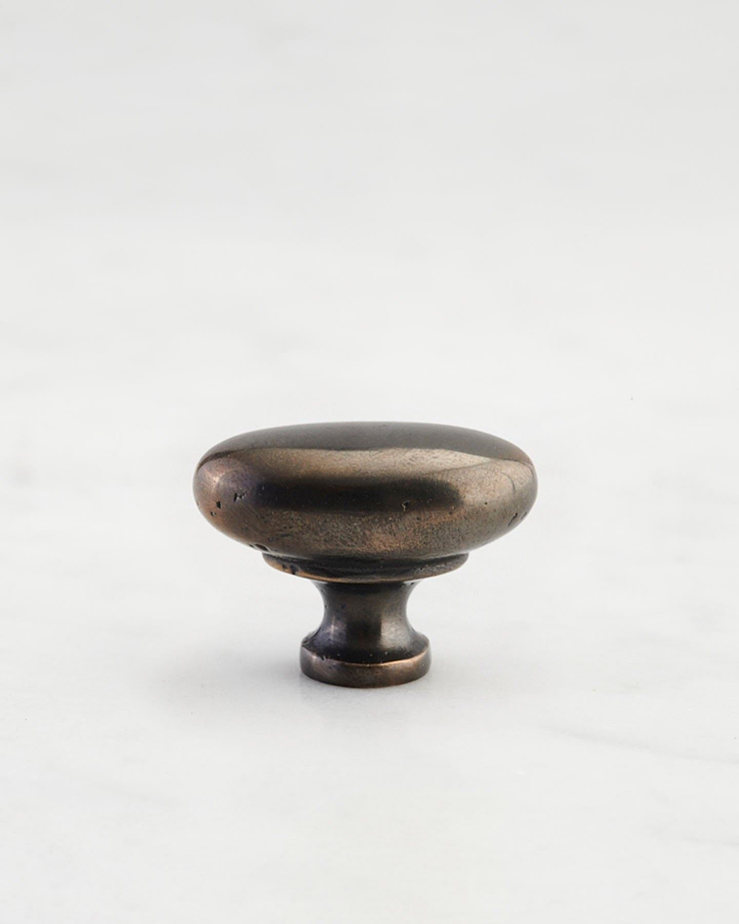 A 'Small' oval-shaped knob for a kitchen cupboard or drawer with a dark oxidised bronze finish and unique dented textures as if was made by an artisan blacksmith centuries ago.