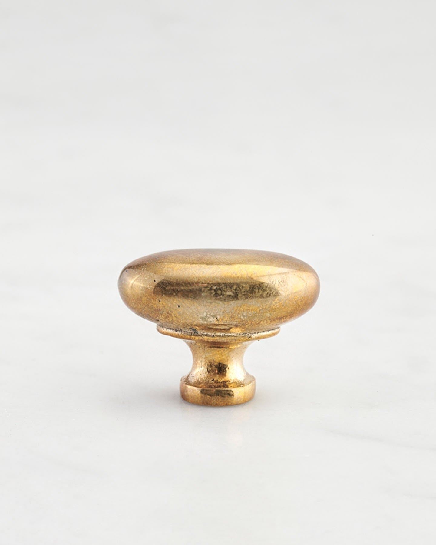 A 'Small' oval-shaped knob for a kitchen cupboard or drawer with a bright polished bronze finish and unique dented textures that makes it look like a beloved, well aged bronze from centuries ago.